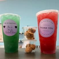 Two colorful smoothie cups with snacks in the middle on a table, one green and one red.