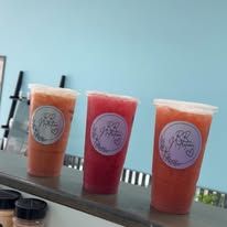Three colorful iced drinks in plastic cups lined up on a table outdoors.