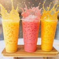 Three colorful smoothies in tall glasses splashing upward on a wooden tray