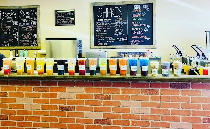 Coffee shop counter with rows of colorful drinks and chalkboard menu signs above a brick front counter