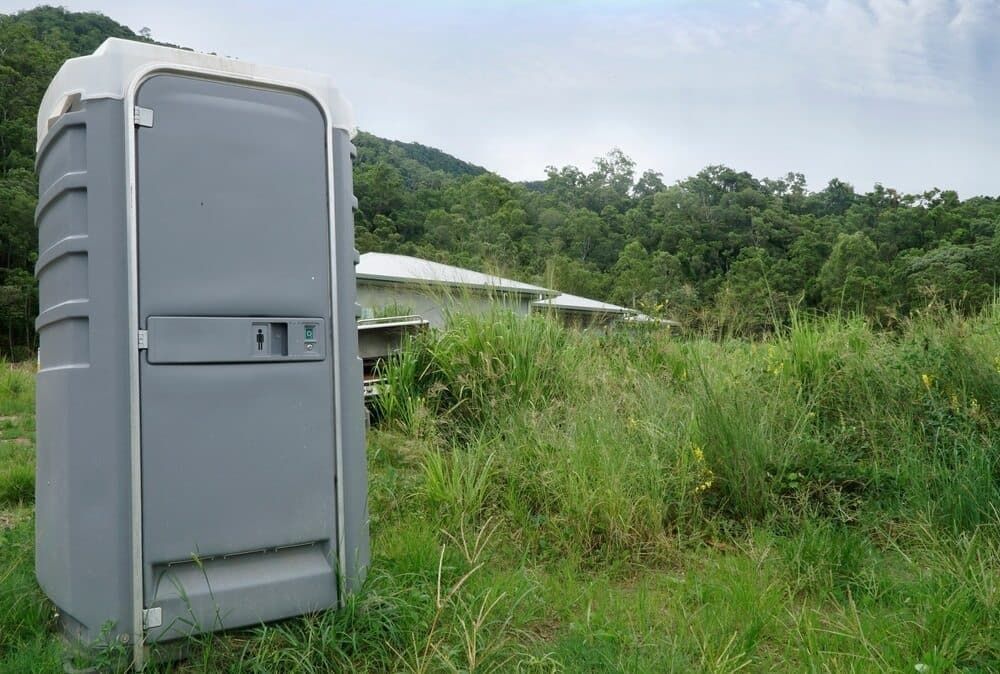 A Portable Toilet is Sitting in the Middle of a Grassy Field — Tony Gordon Septic Tank Cleaning in Newee Creek, NSW