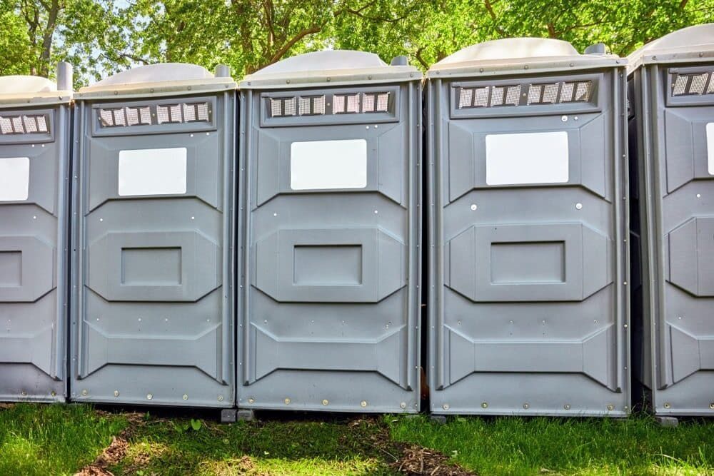 A Row of Portable Toilets Are Lined Up in a Grassy Field — Tony Gordon Septic Tank Cleaning in Newee Creek, NSW