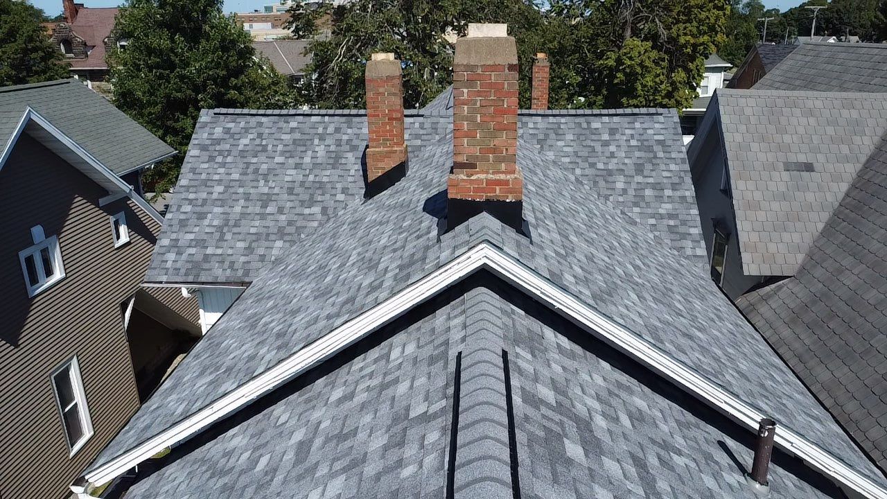 Gray shingled roof with two brick chimneys, seen from above, in a residential neighborhood.
