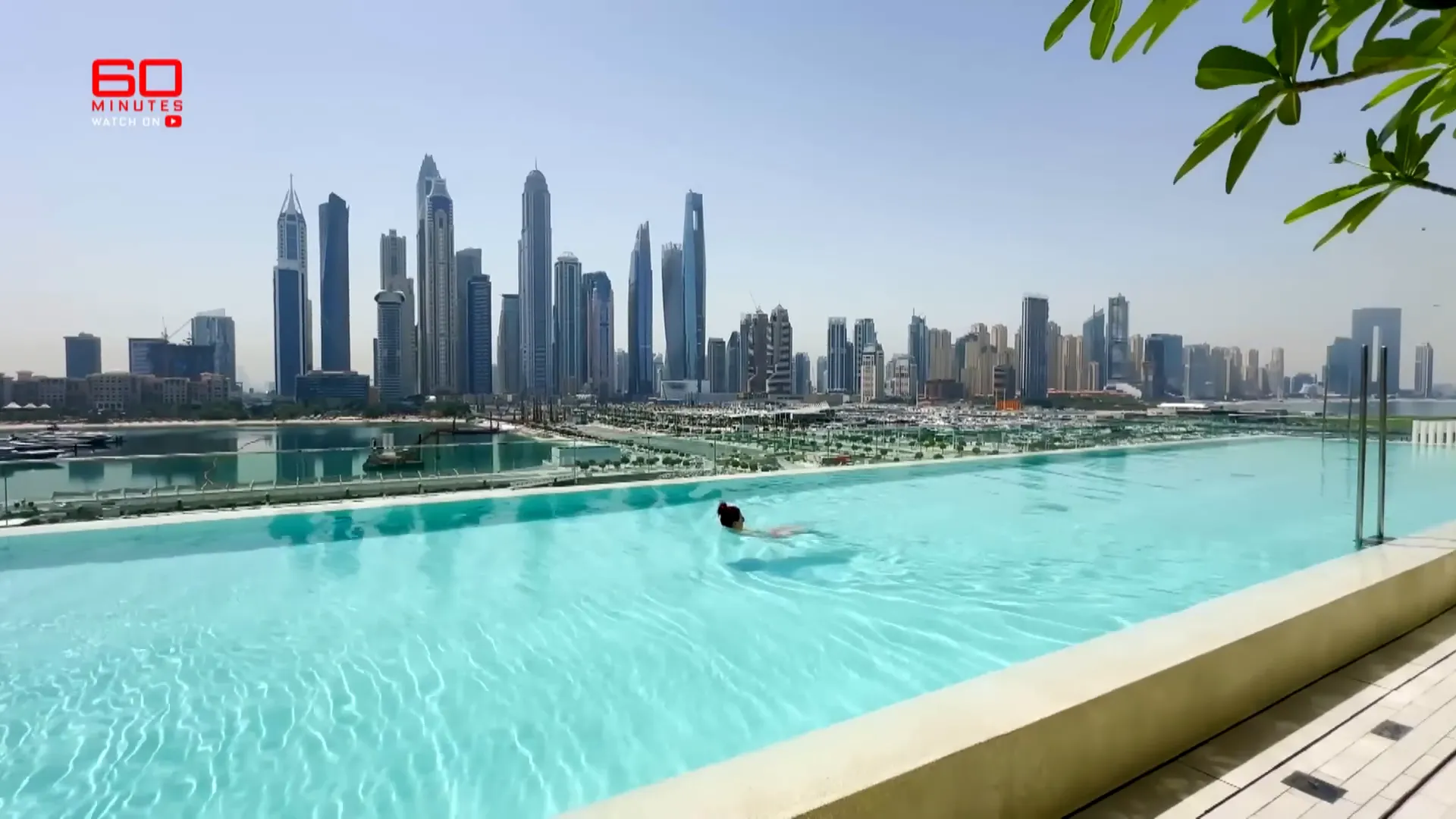 A person is swimming in an infinity pool with a city skyline in the background.