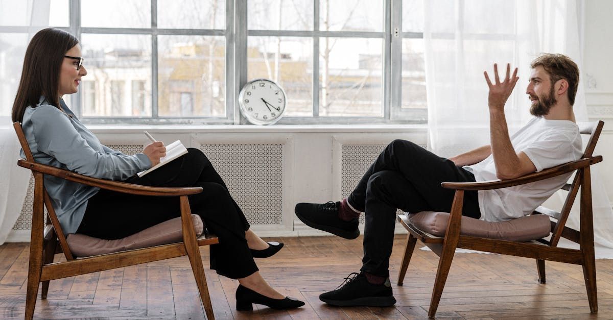 A man and a woman are sitting in chairs talking to each other. Psychologists.