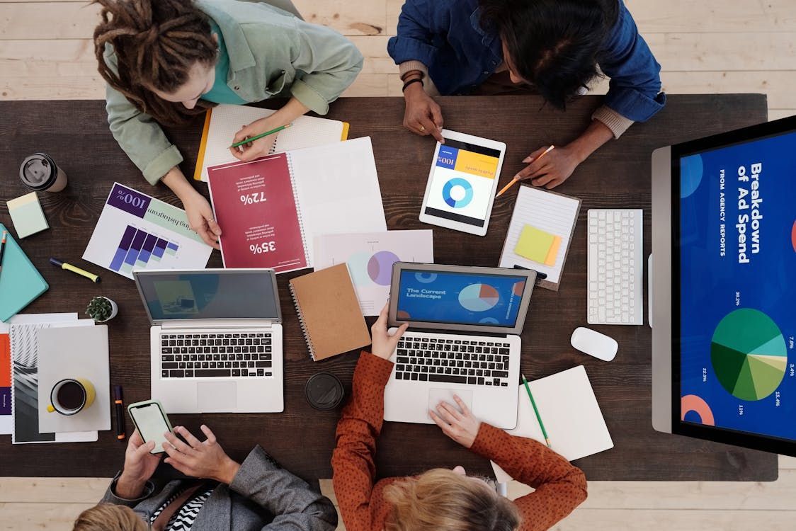 A group of people are sitting around a table with laptops and papers.