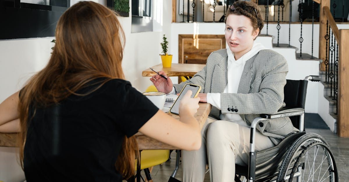 A woman in a wheelchair is sitting at a table talking to another woman.