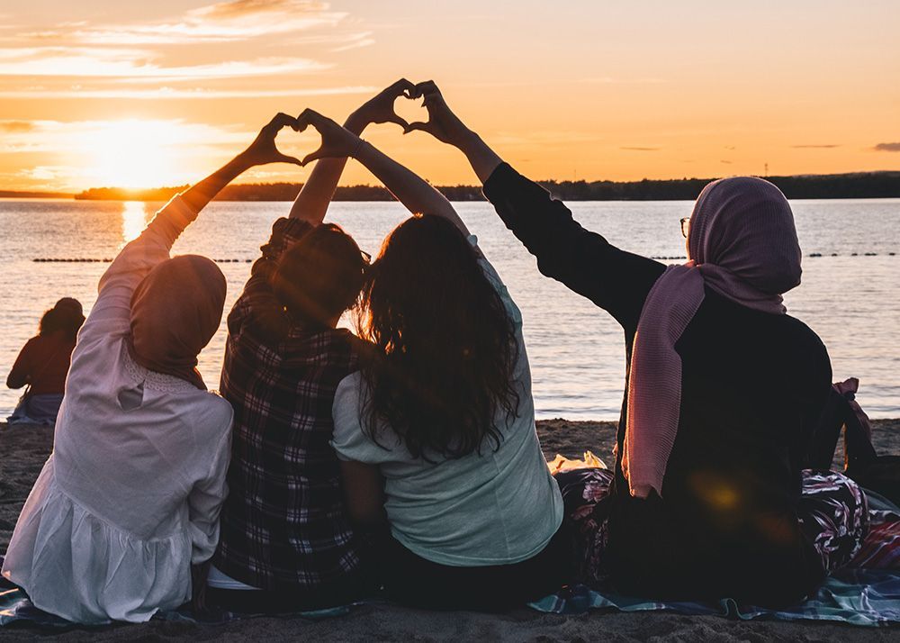 people holding hands in the air as friends making heart shapes at sunset