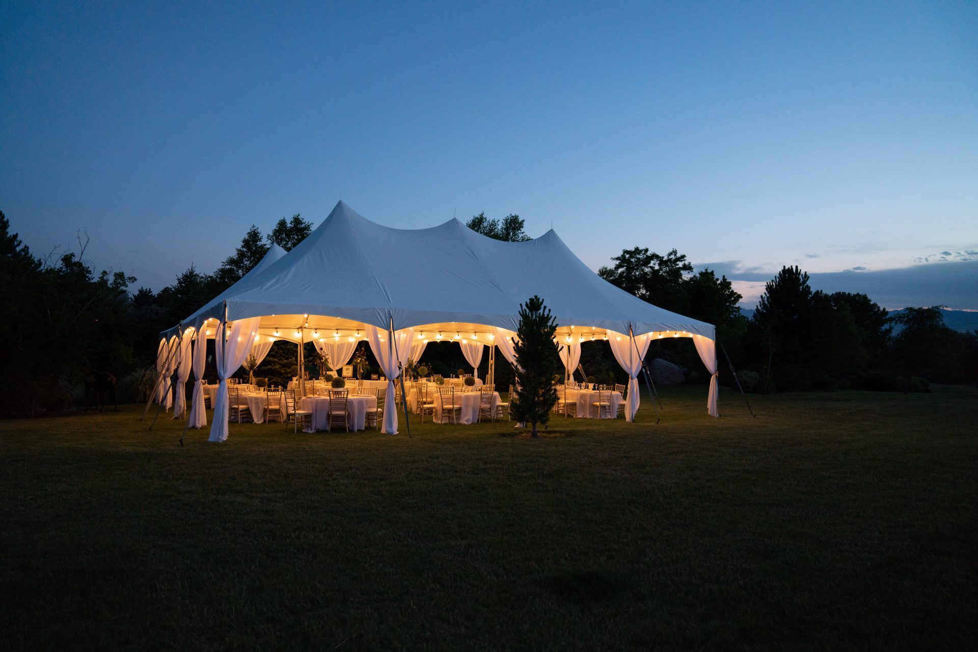 Memorial Mortuaries Celebration of life tent set up with tables, chairs and flowers at night with lights on
