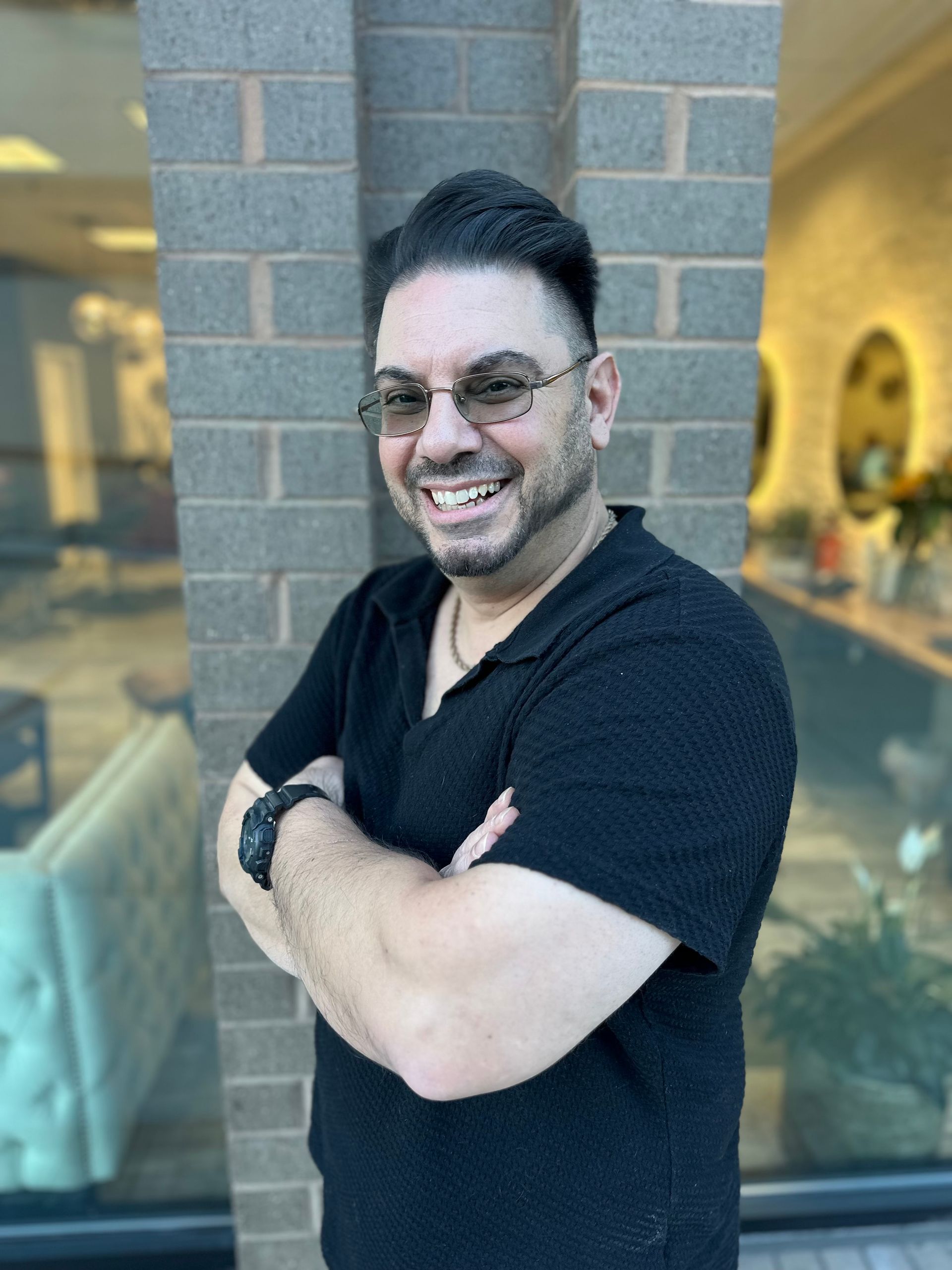 A man in a black shirt is smiling in front of a grassy field.