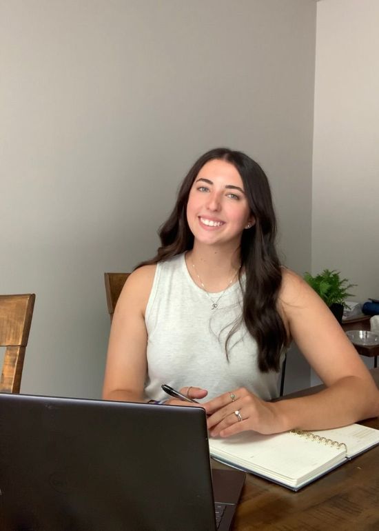 A woman is sitting at a desk with a laptop and a vase of flowers.