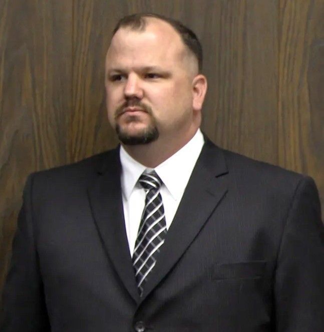 A man in a suit and tie is standing in front of a wooden wall.