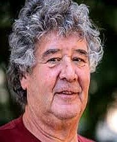 A man with curly hair is wearing a red shirt and smiling for the camera.