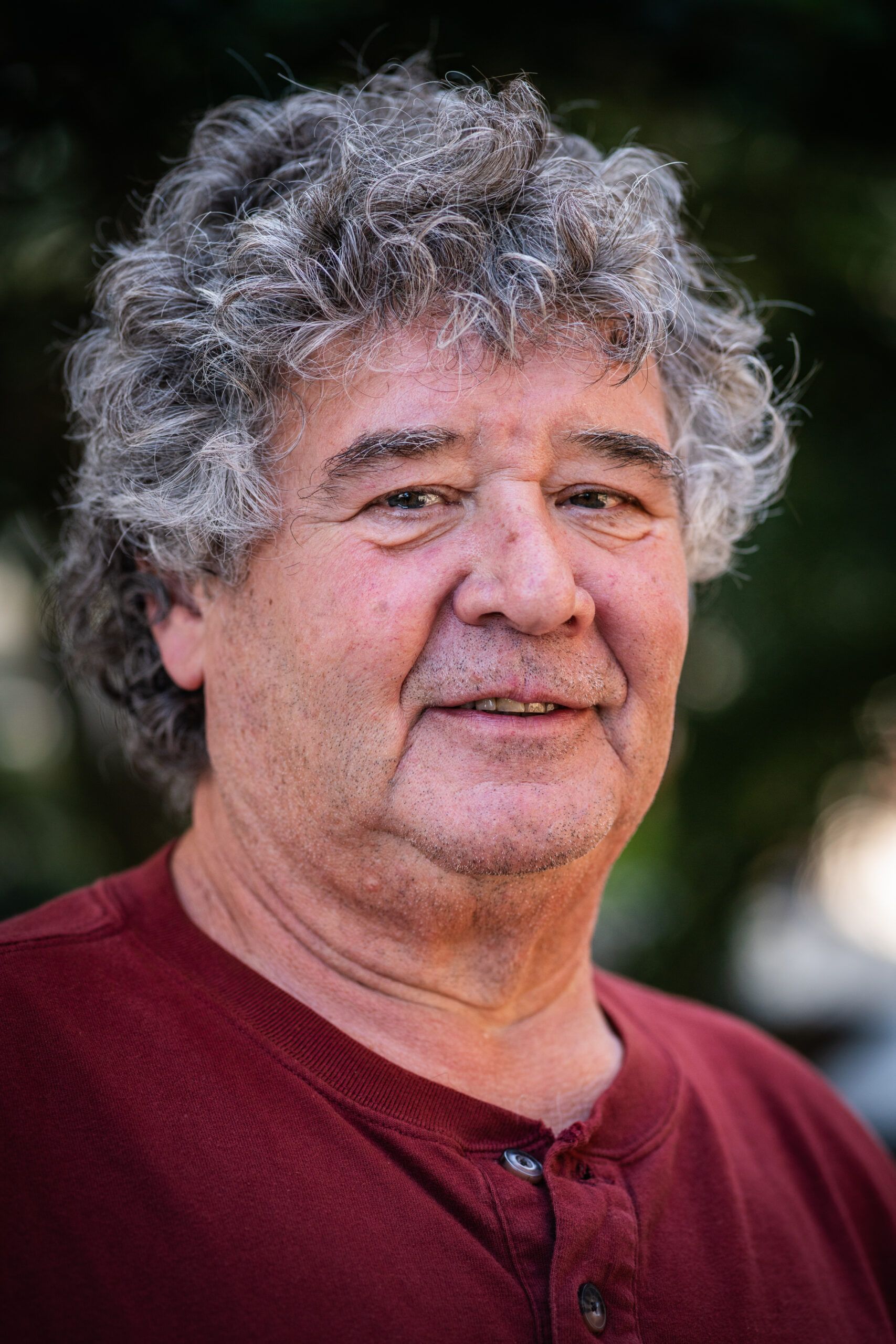 A man with curly hair is wearing a red shirt and smiling for the camera.