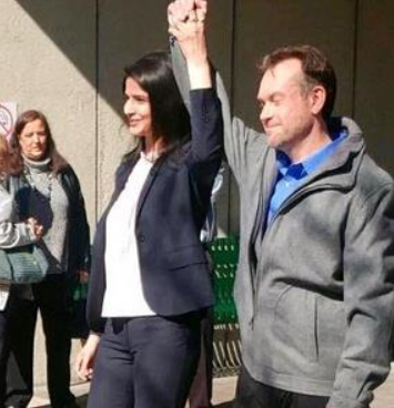 A man and a woman are standing next to each other and the woman is raising her fist in the air