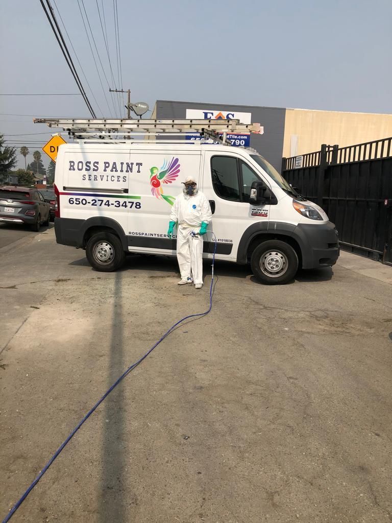 A man in a protective suit is spraying a van with a hose.