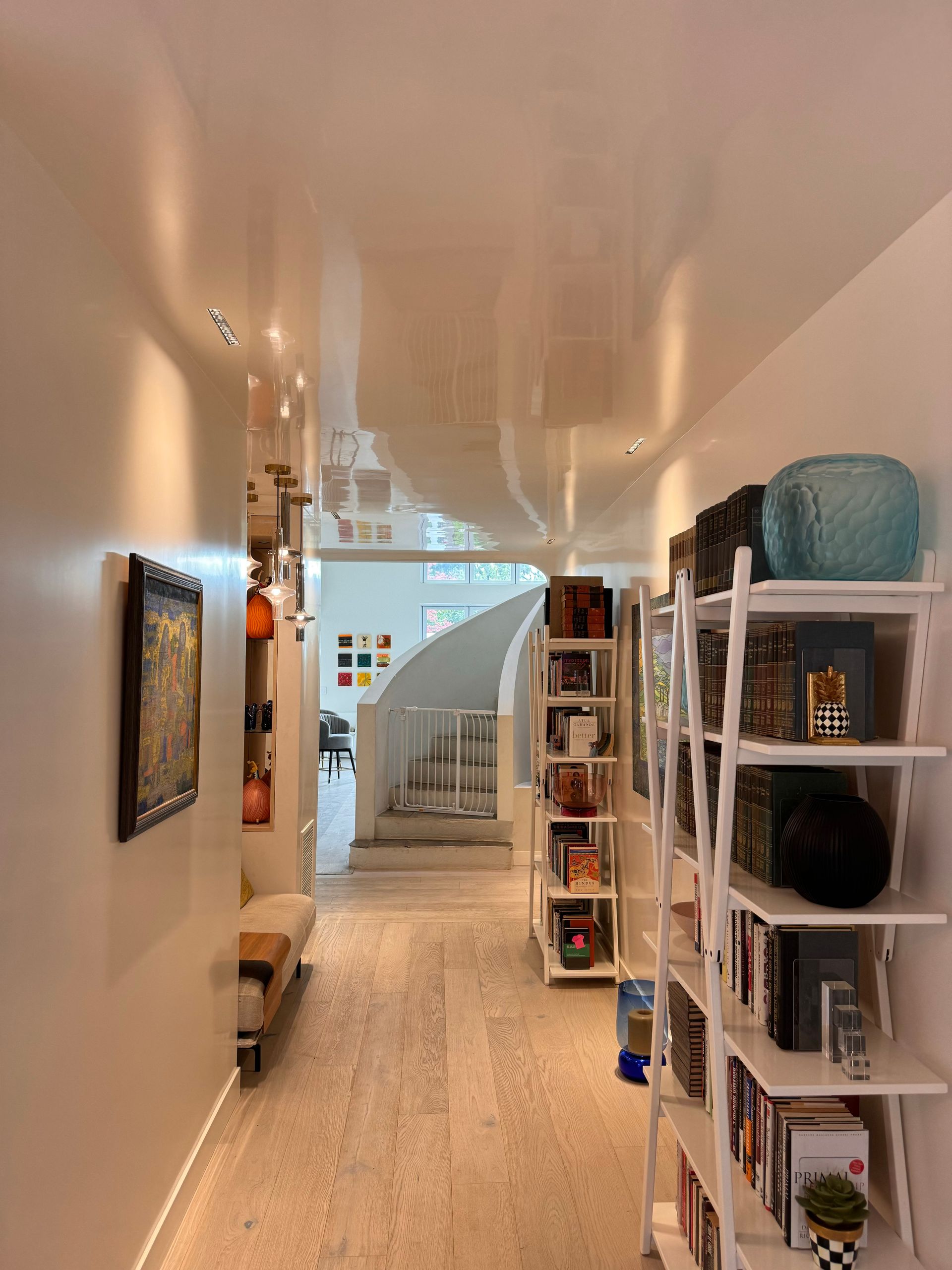 Long hallway with white walls, shelves of books, and a spiral staircase in the distance.