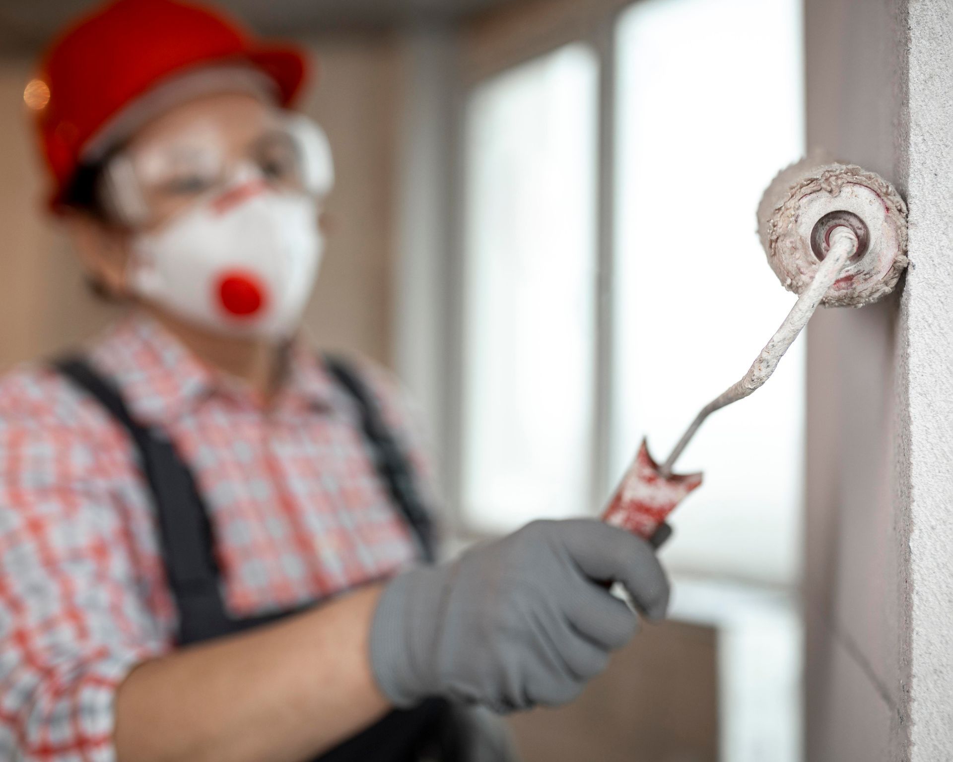 A man wearing a mask and gloves is painting a wall with a paint roller.