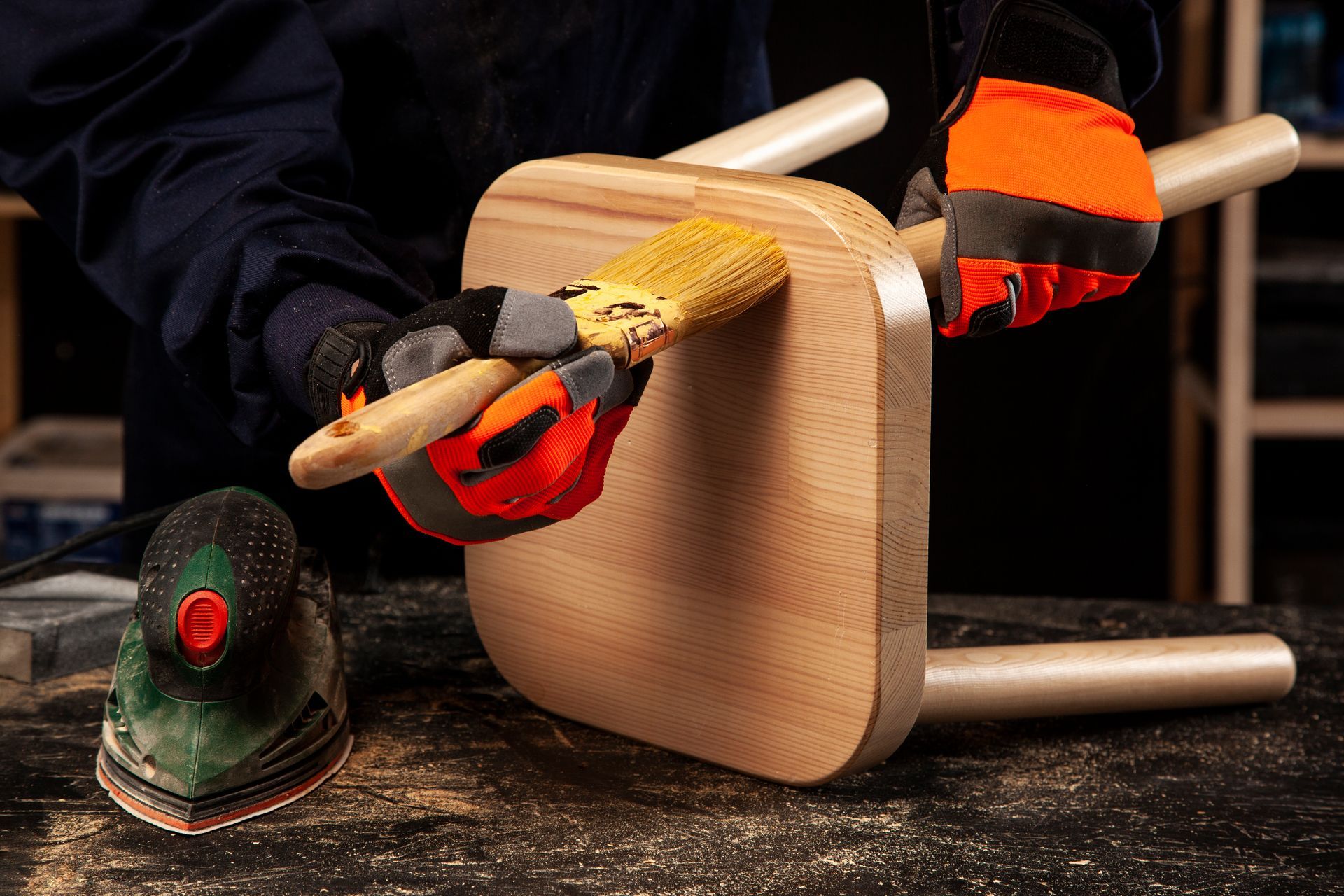 A person is sanding a wooden stool with a sander.