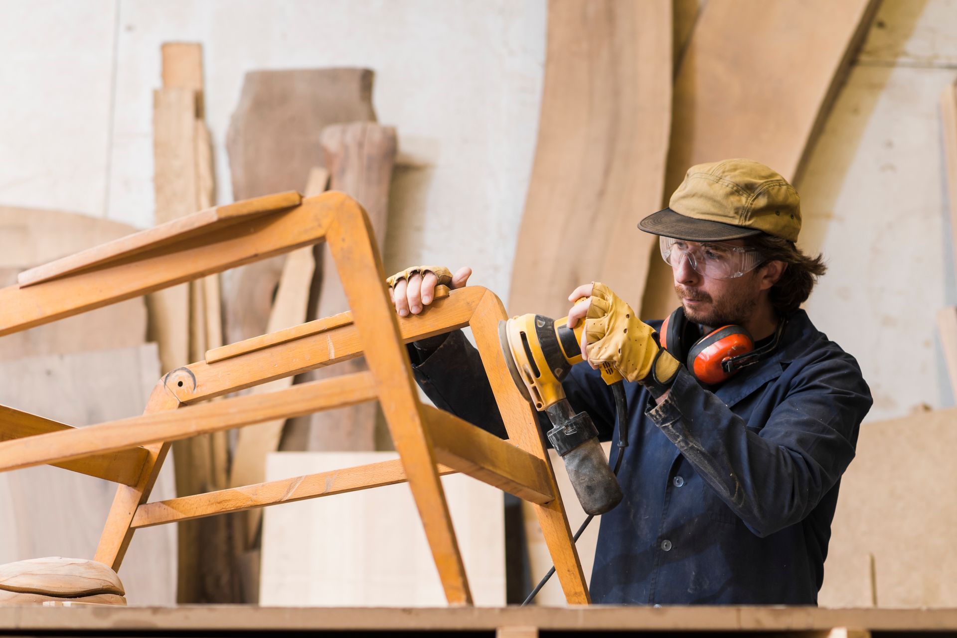 A man is sanding a wooden chair in a workshop.