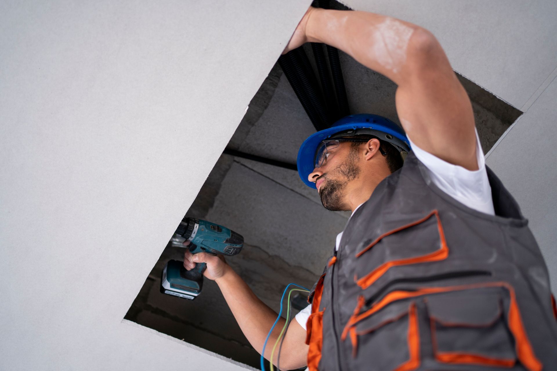 A man is using a drill to fix a hole in the ceiling.