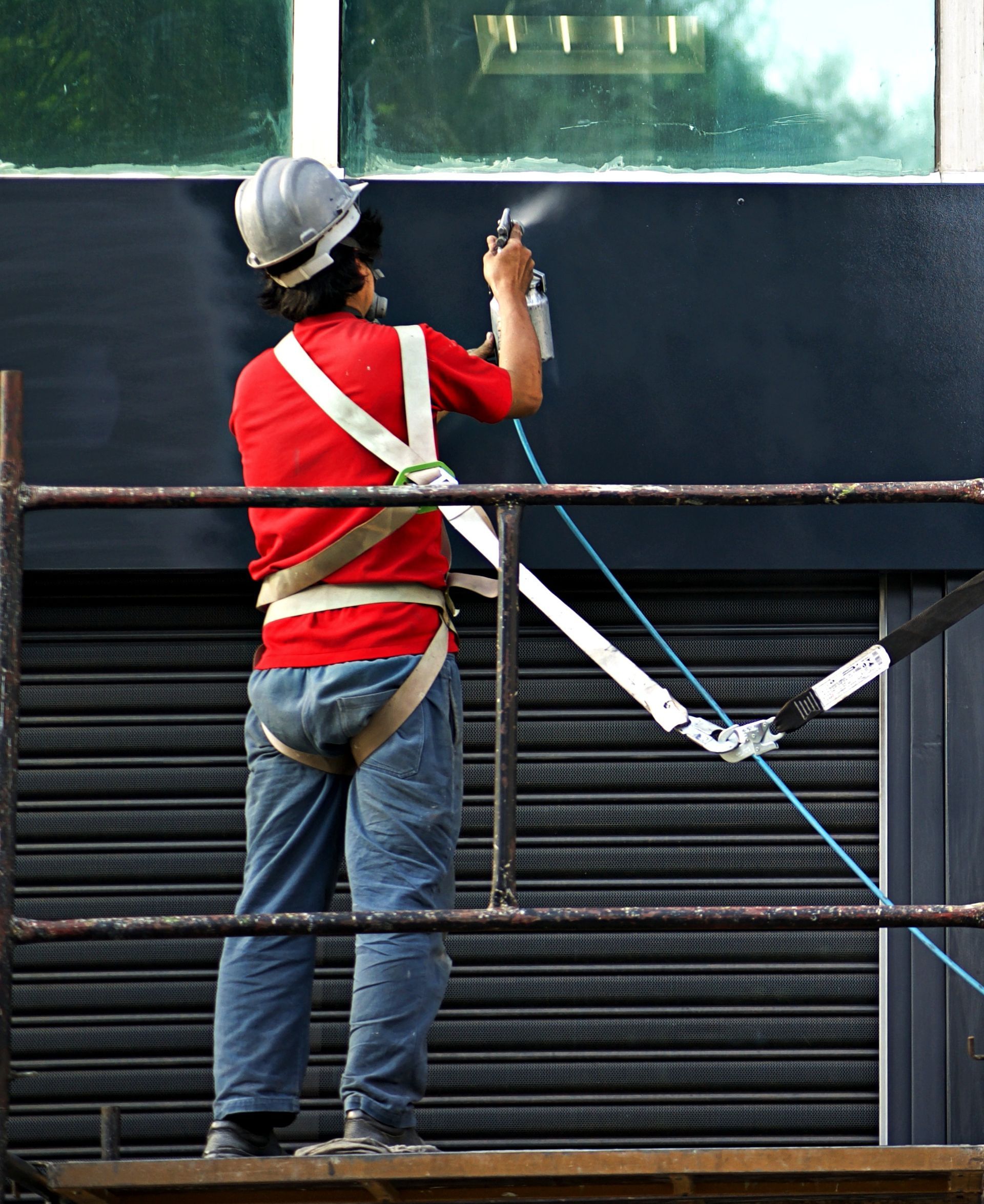 A man in a red shirt is spraying paint on a building