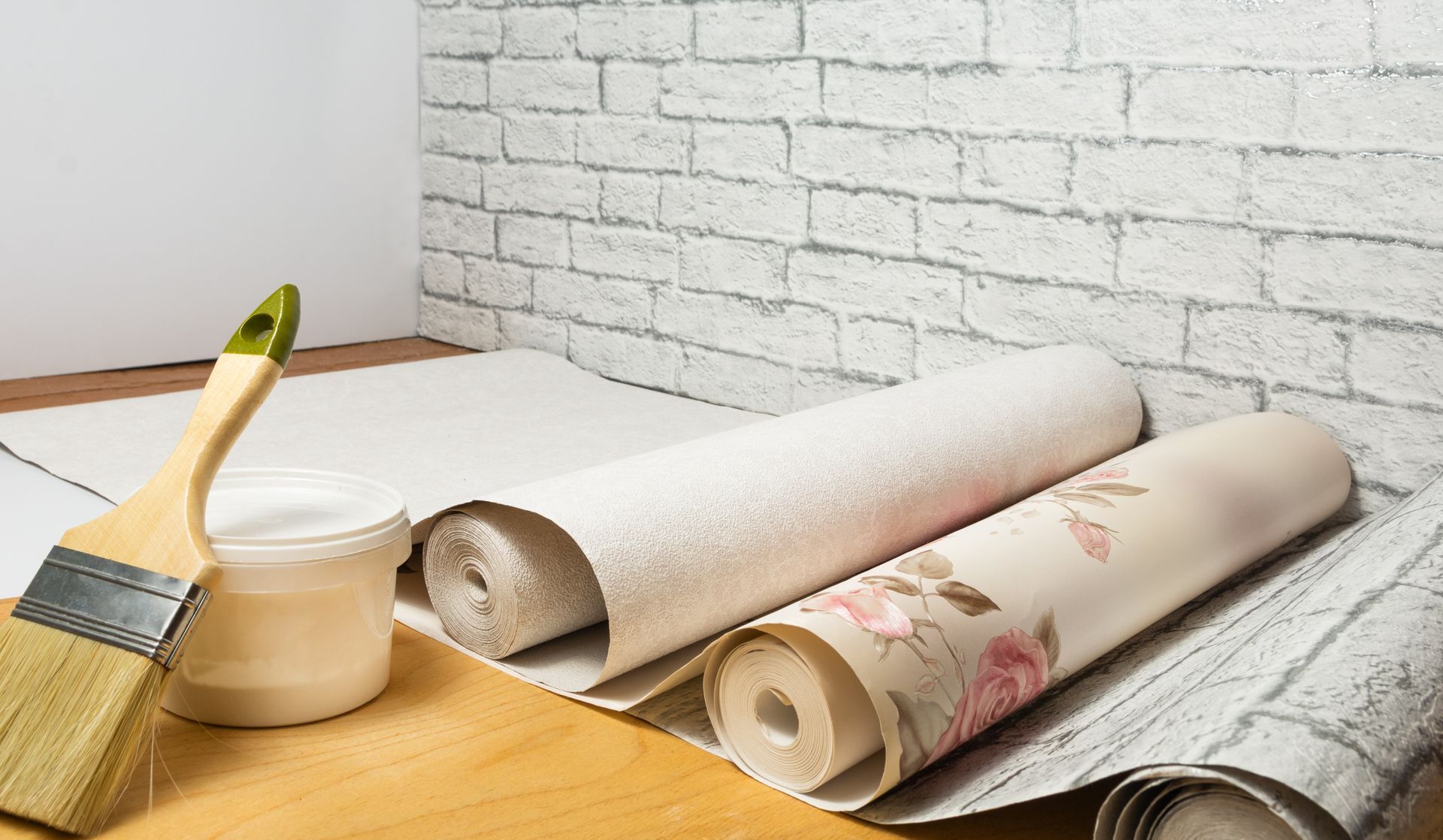 Rolls of wallpaper , a brush , and a bucket of glue are sitting on a wooden table.