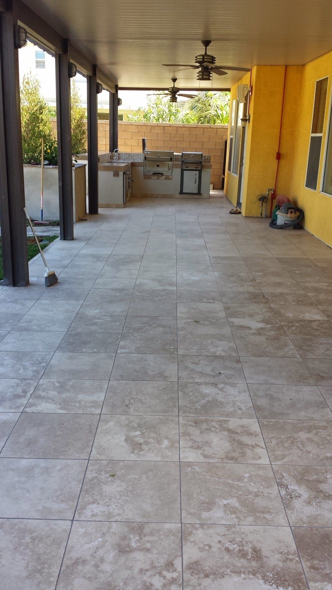 A large patio with a ceiling fan and a grill