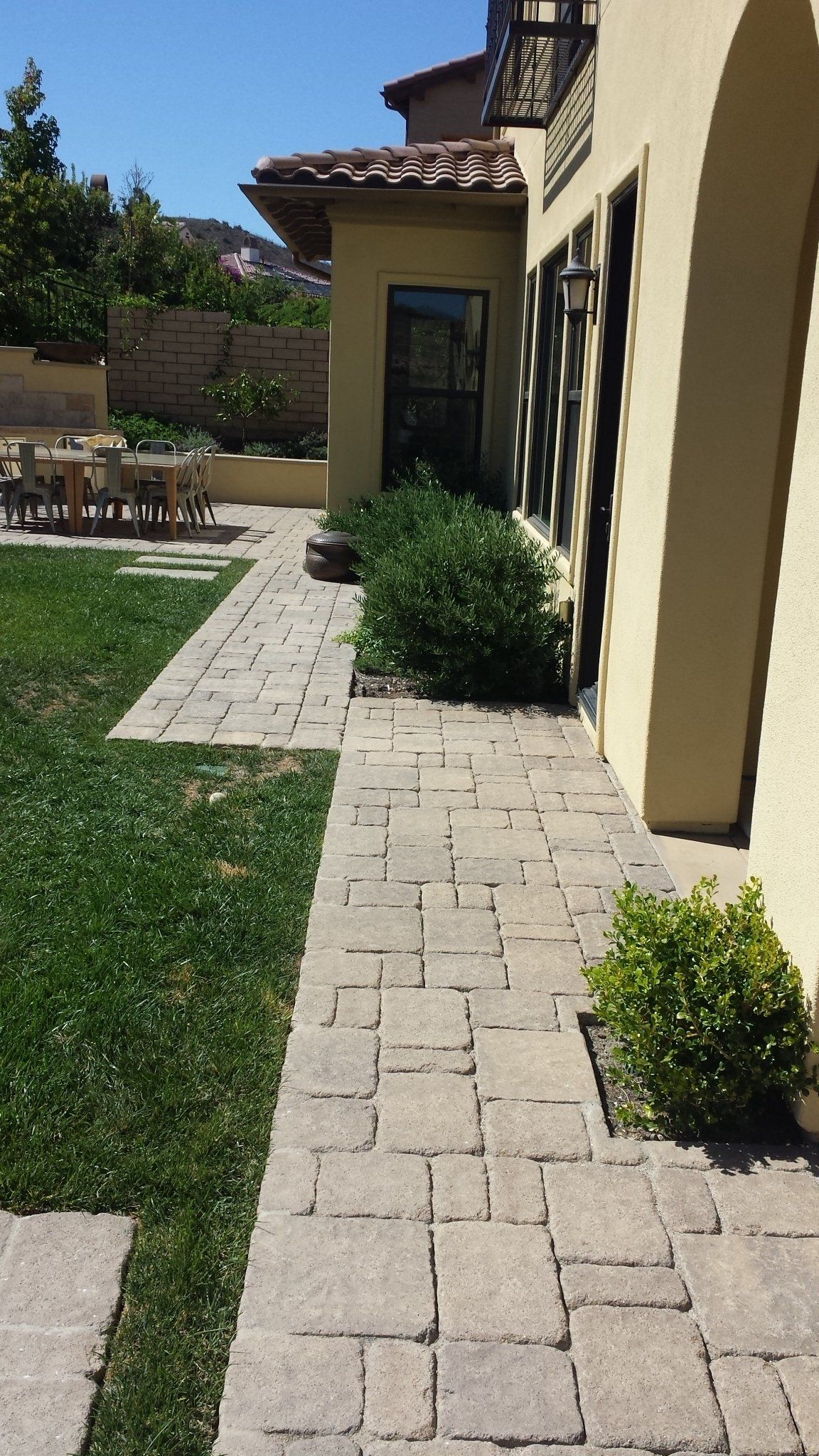 A brick walkway leading to a house with a lawn in the background