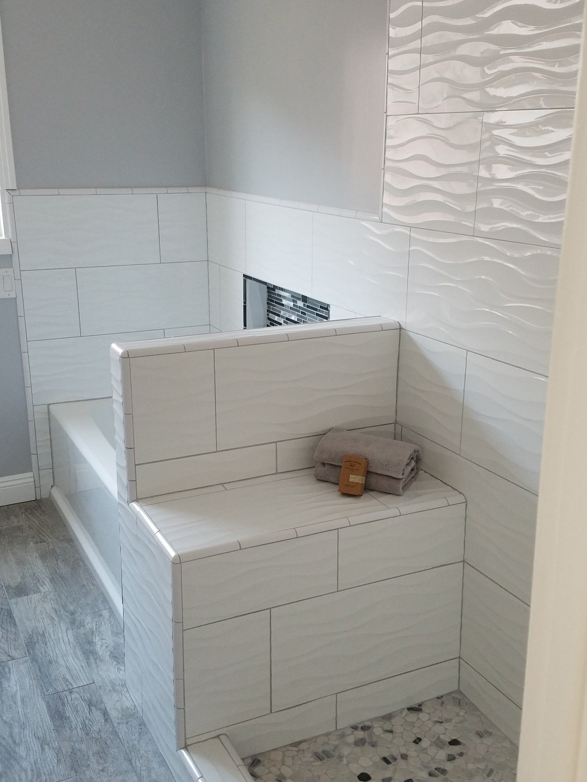 A bathroom with white tiles and a bench in the corner.