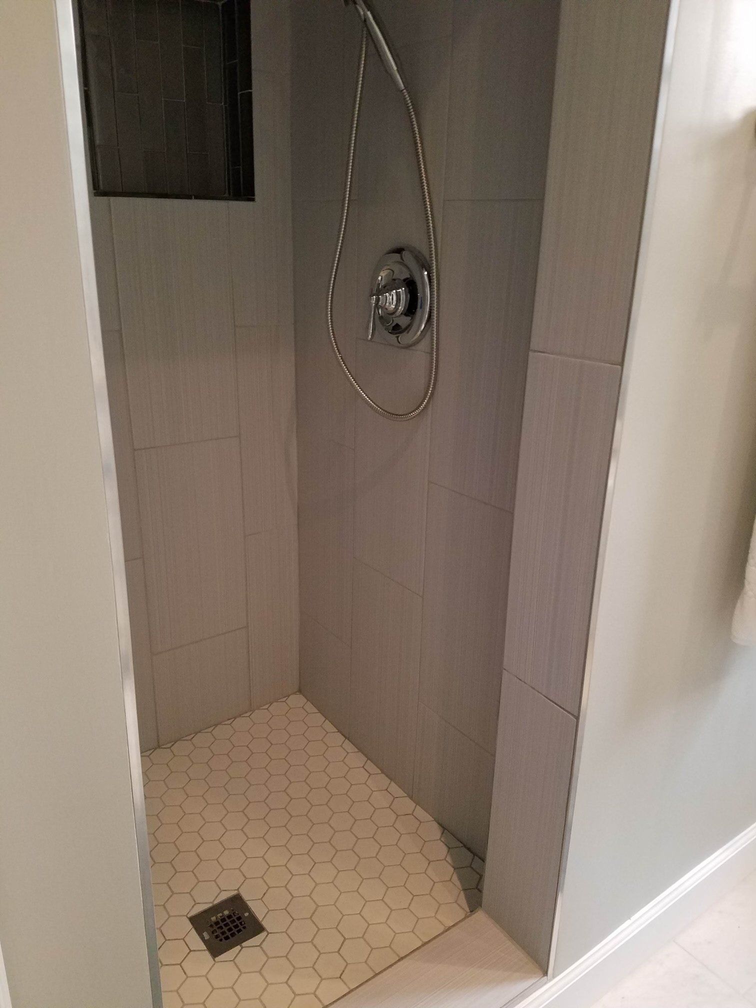 A shower stall with a shower head and drain in a bathroom.