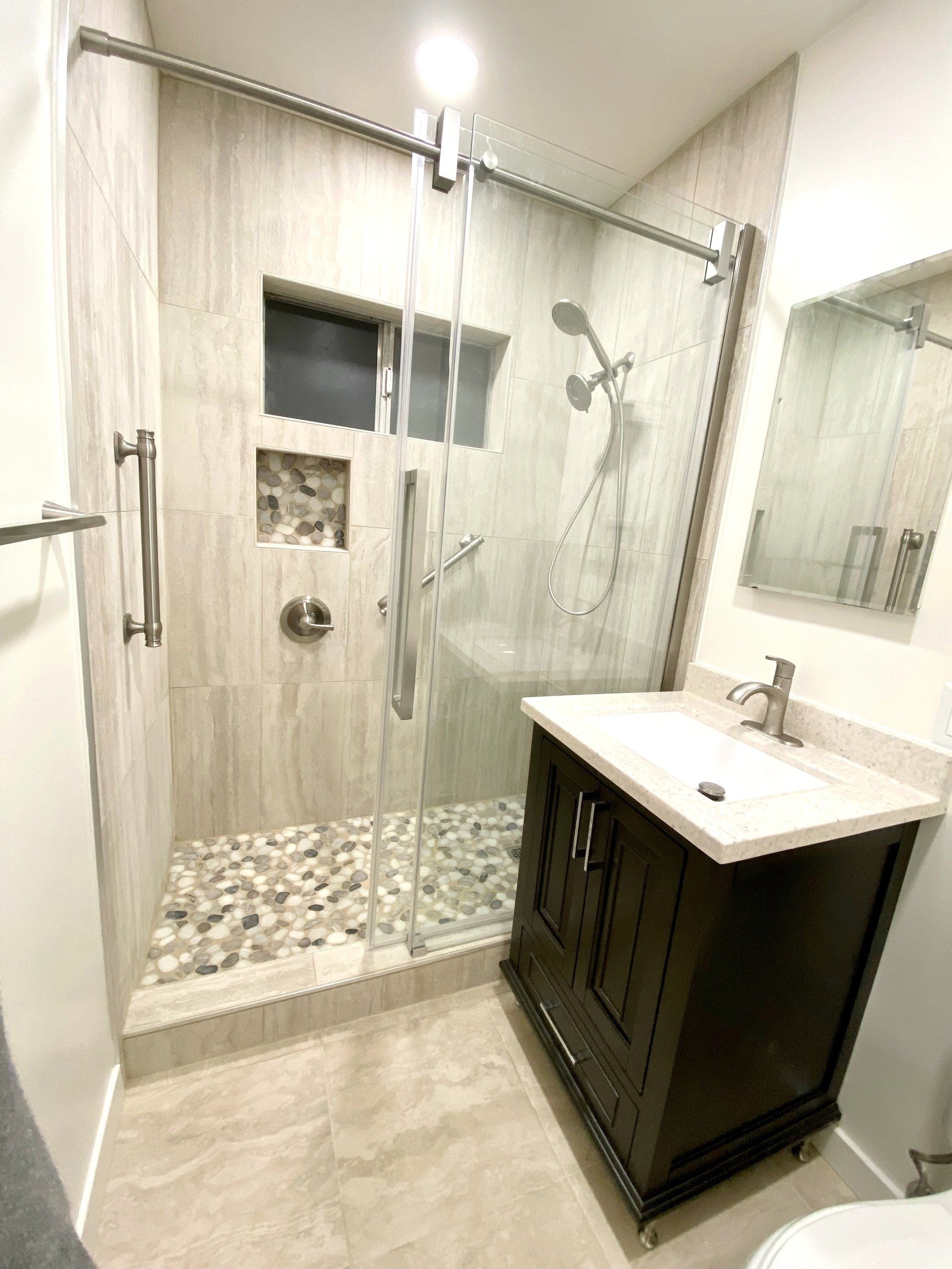 A bathroom with a walk in shower , sink , toilet and mirror.