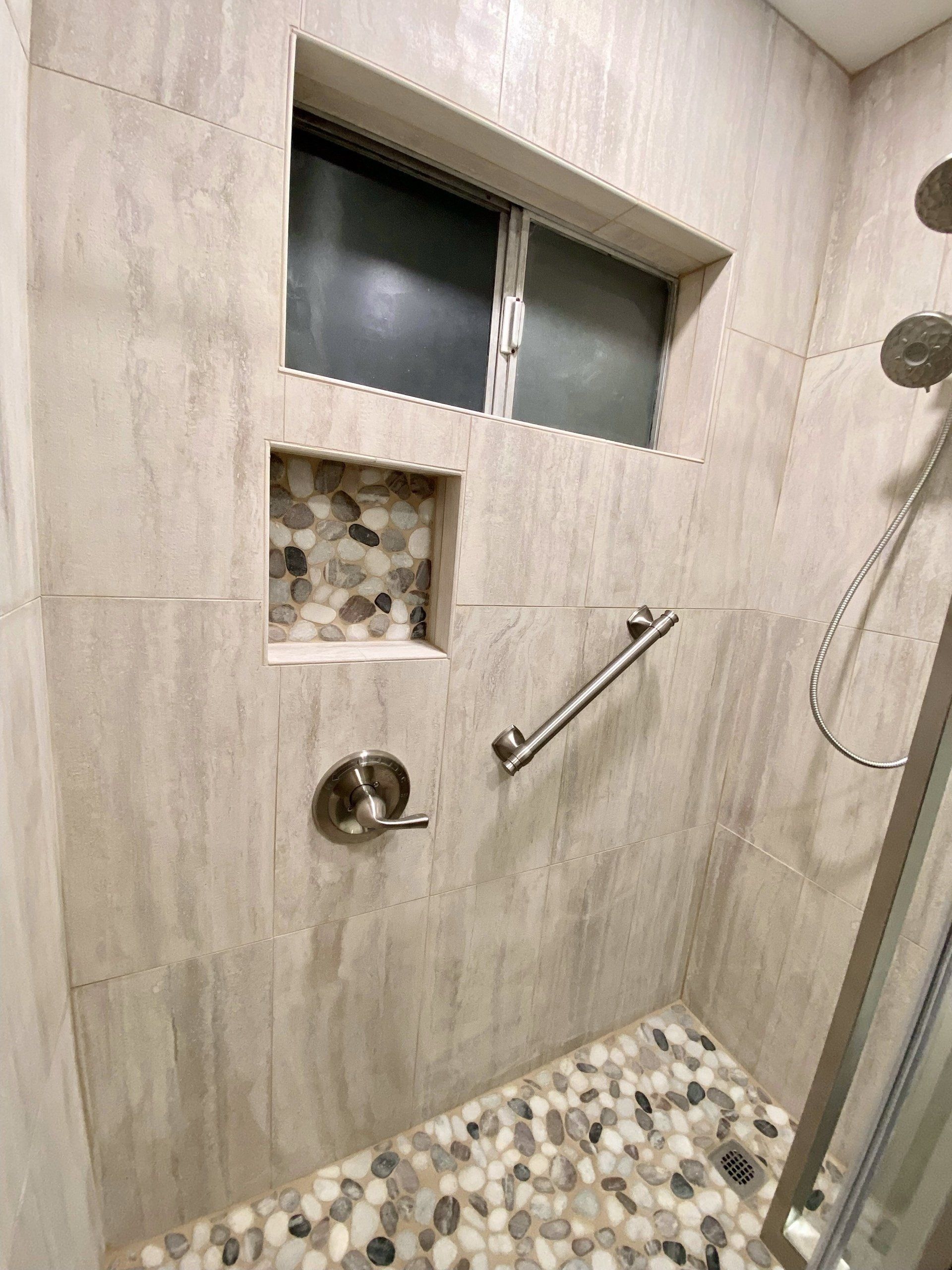 A walk in shower with a window and a hand rail.