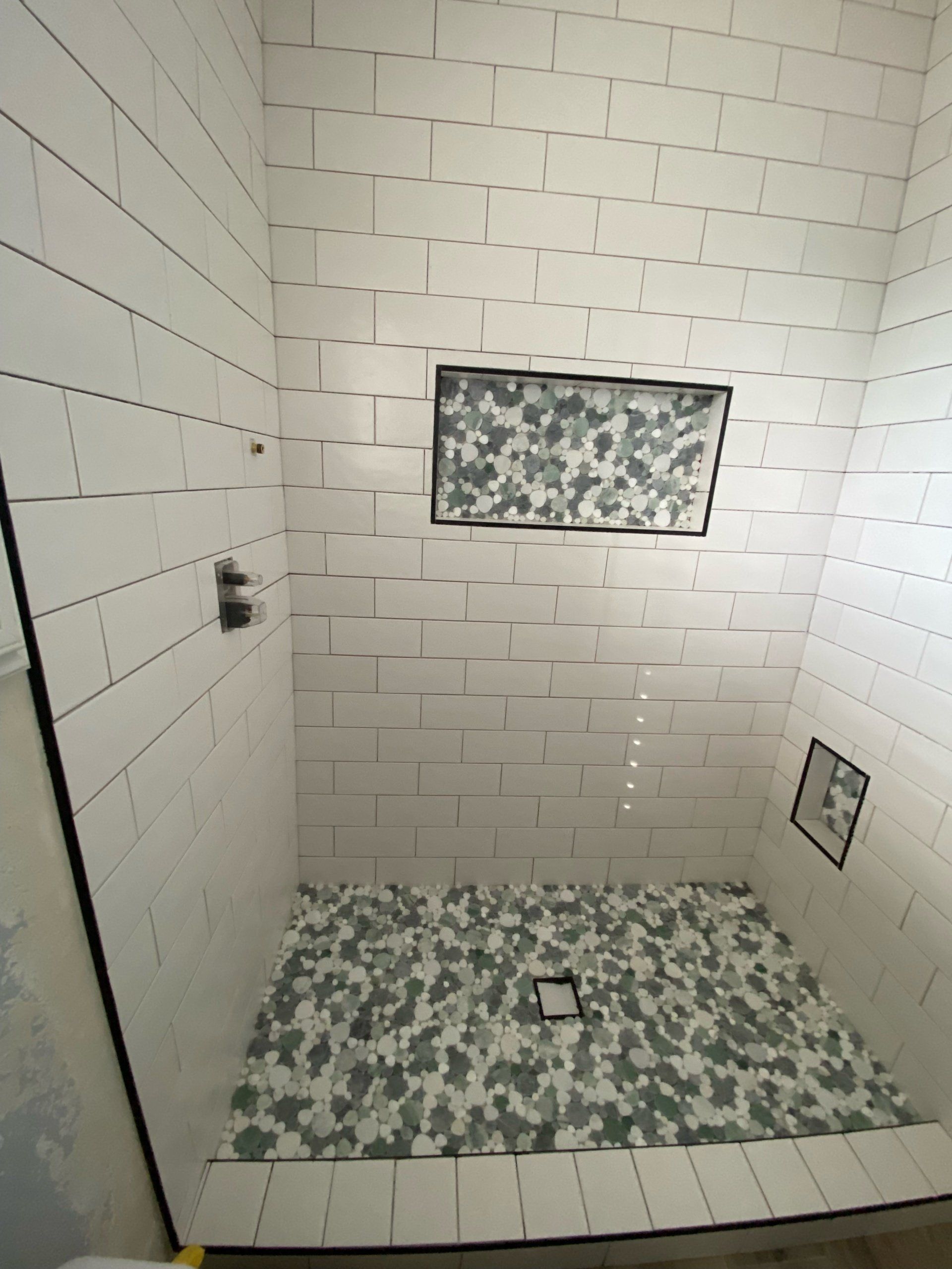 A shower stall with white tiles and a mosaic floor