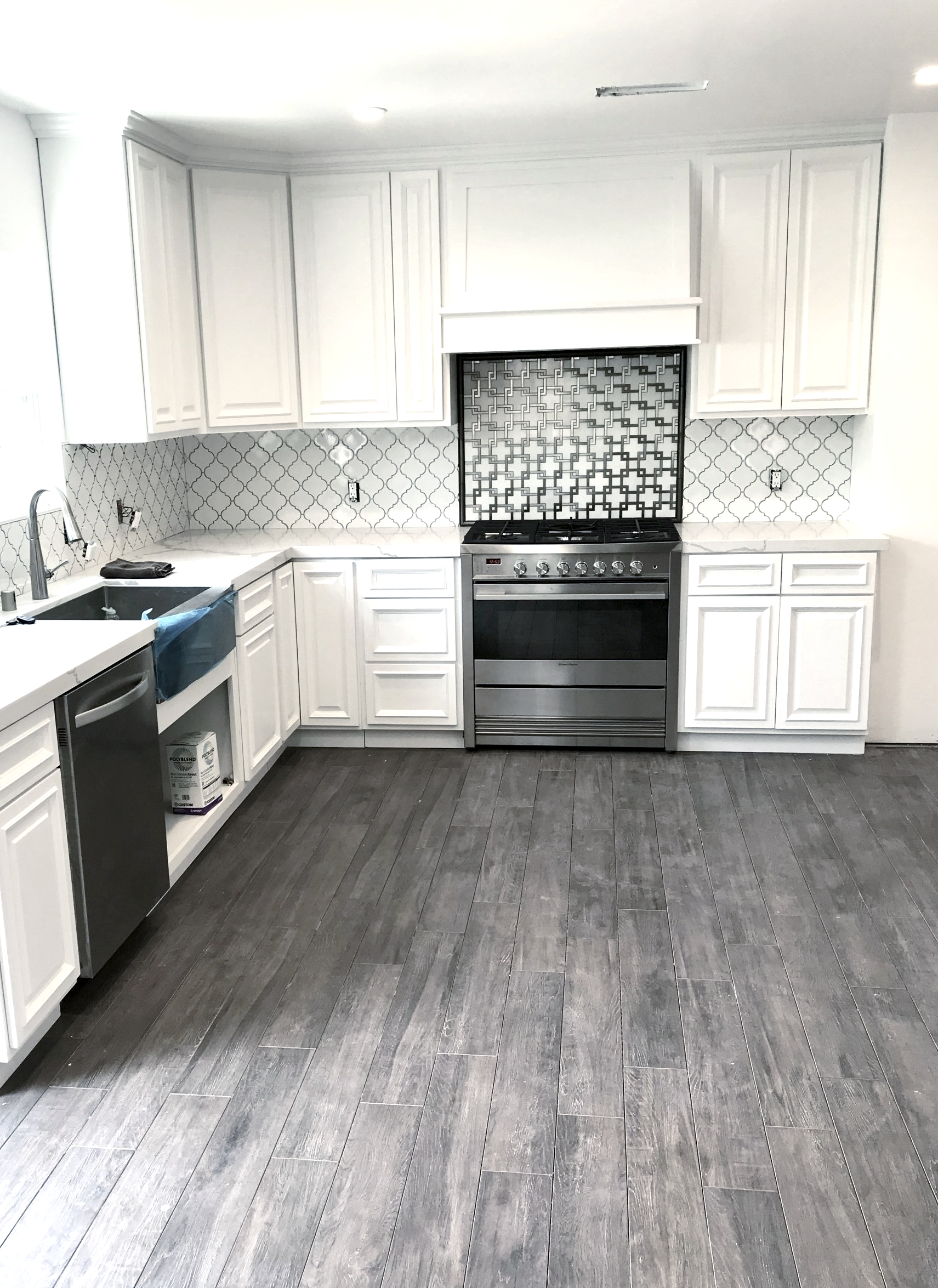 A kitchen with white cabinets , a stove , a sink and a dishwasher.