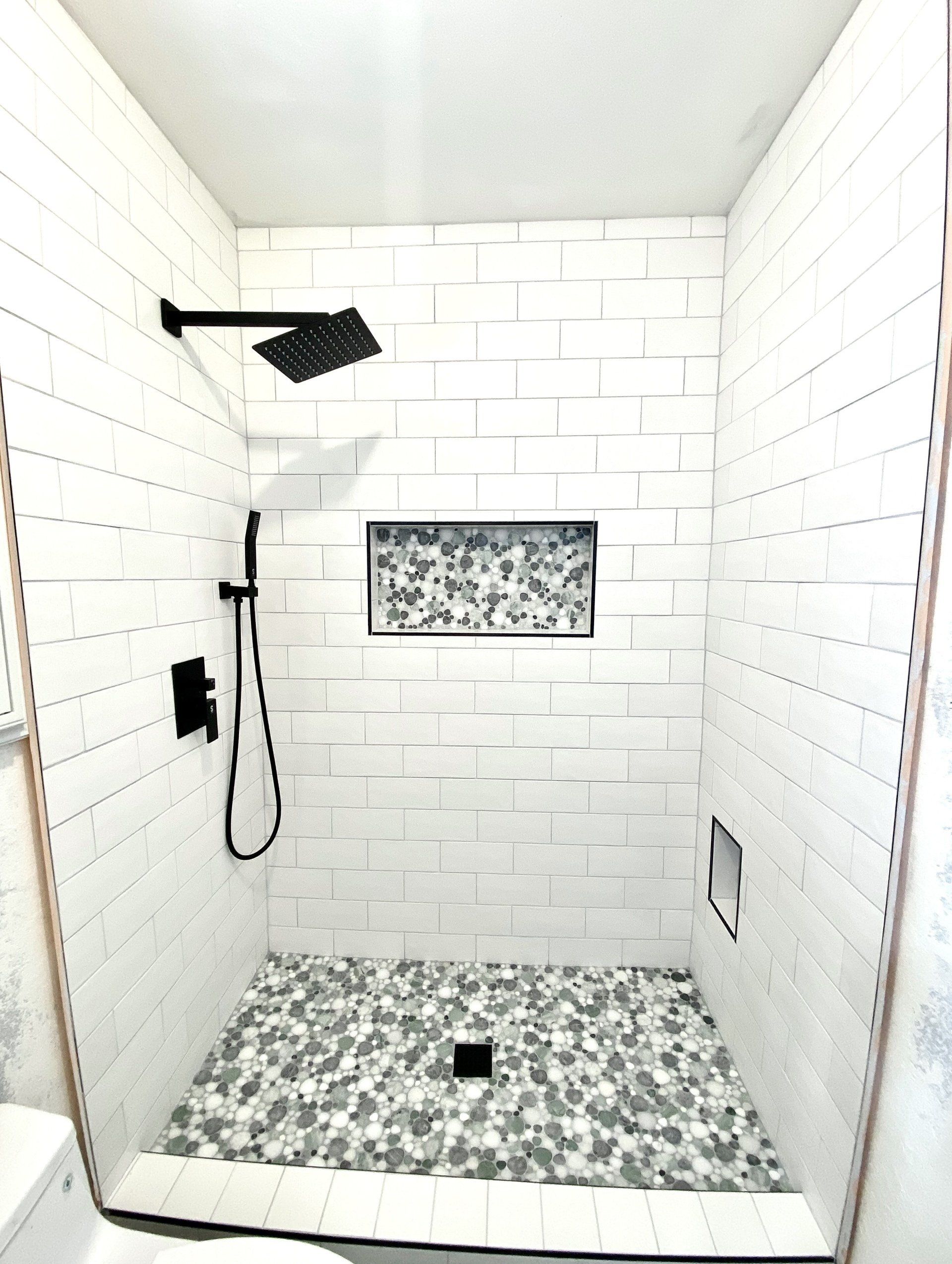 A shower stall with white tiles and a black shower head.