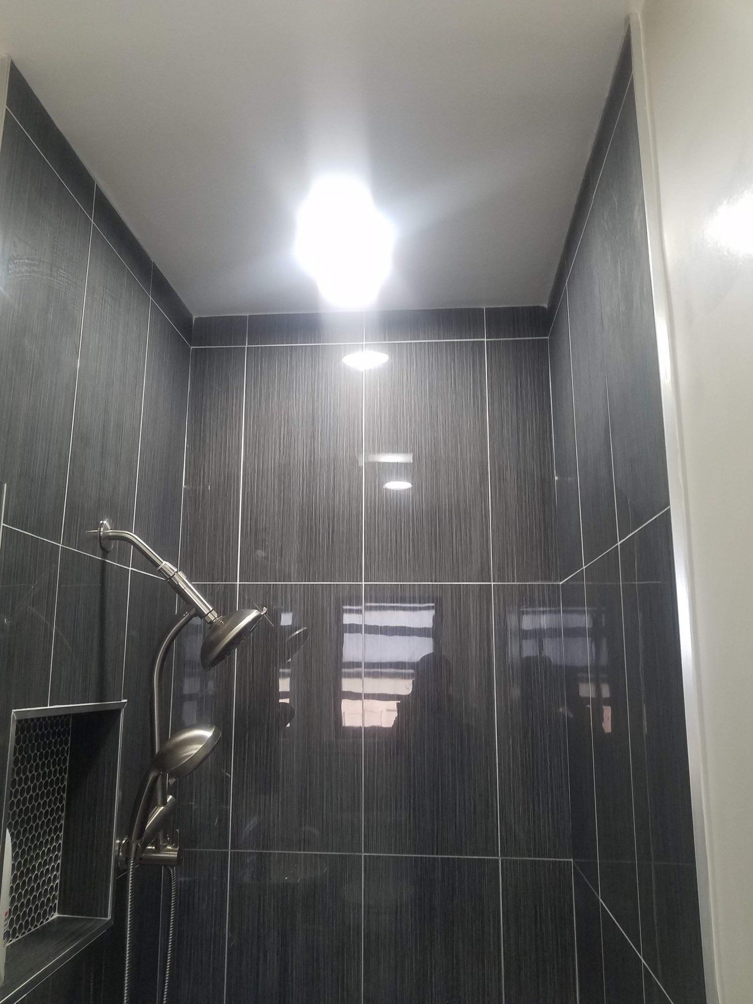 A bathroom with black tiles and a shower head.