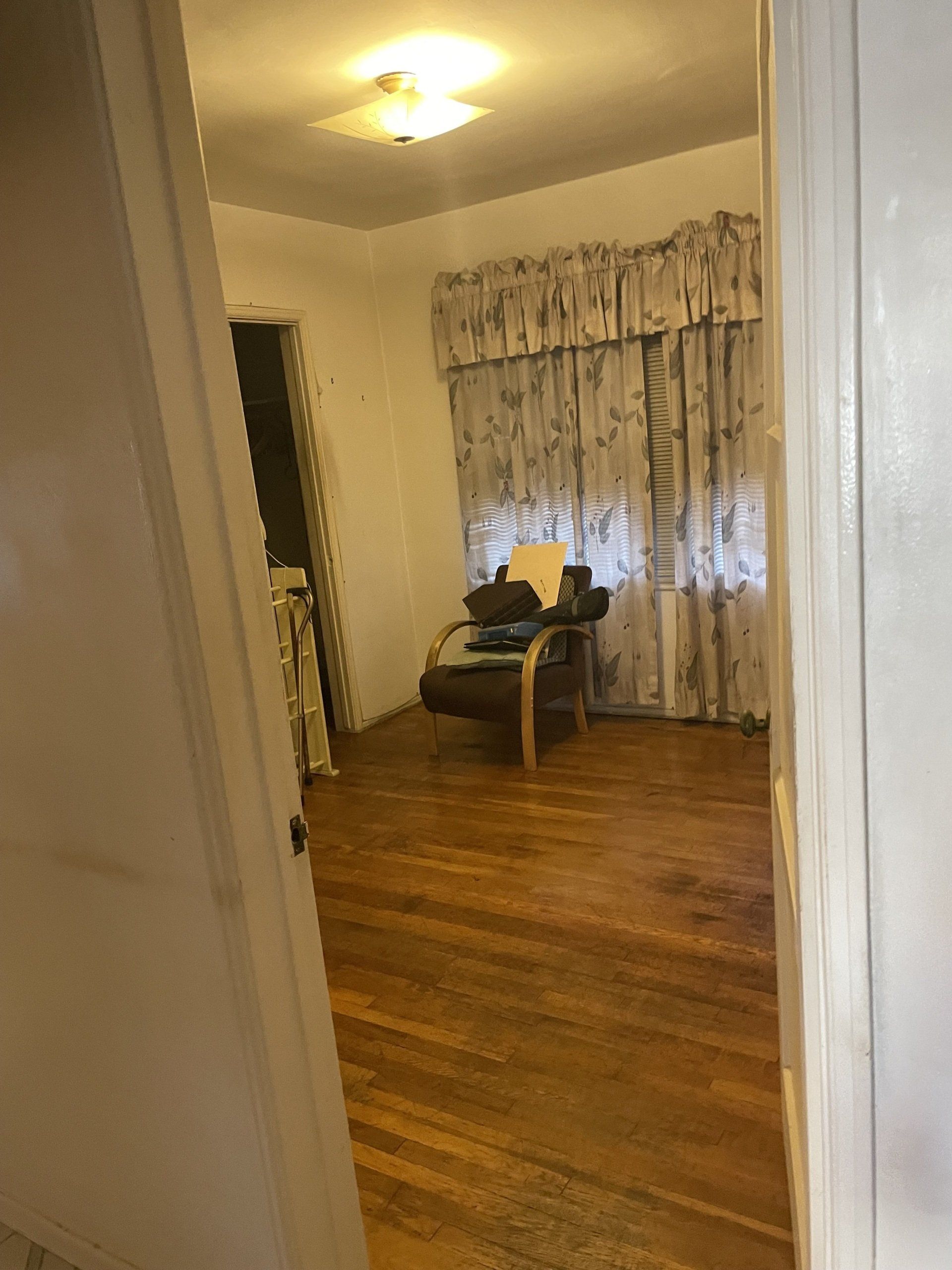 A living room with hardwood floors , a chair , a table and curtains.