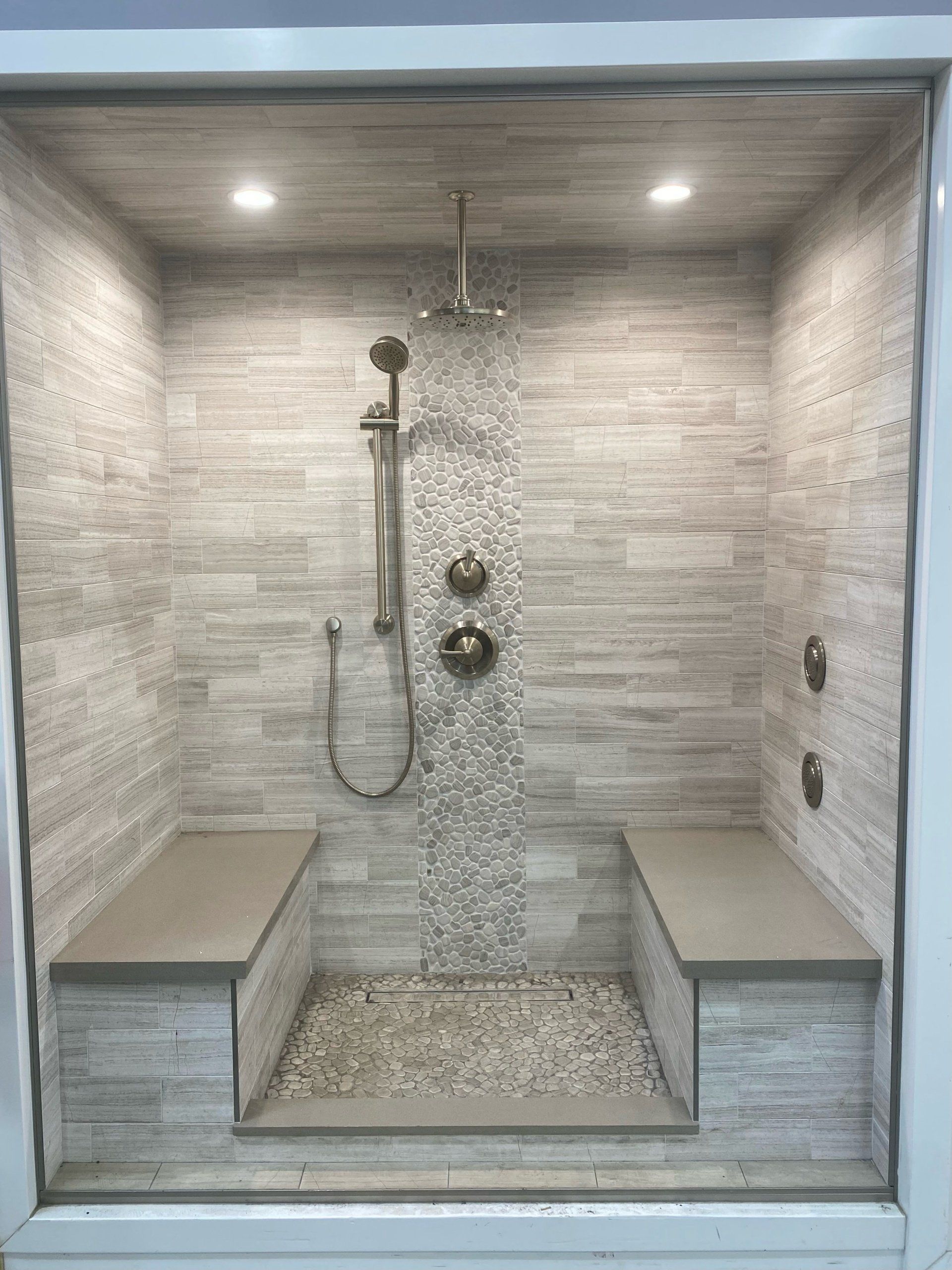 A walk in shower with two benches and a shower head.