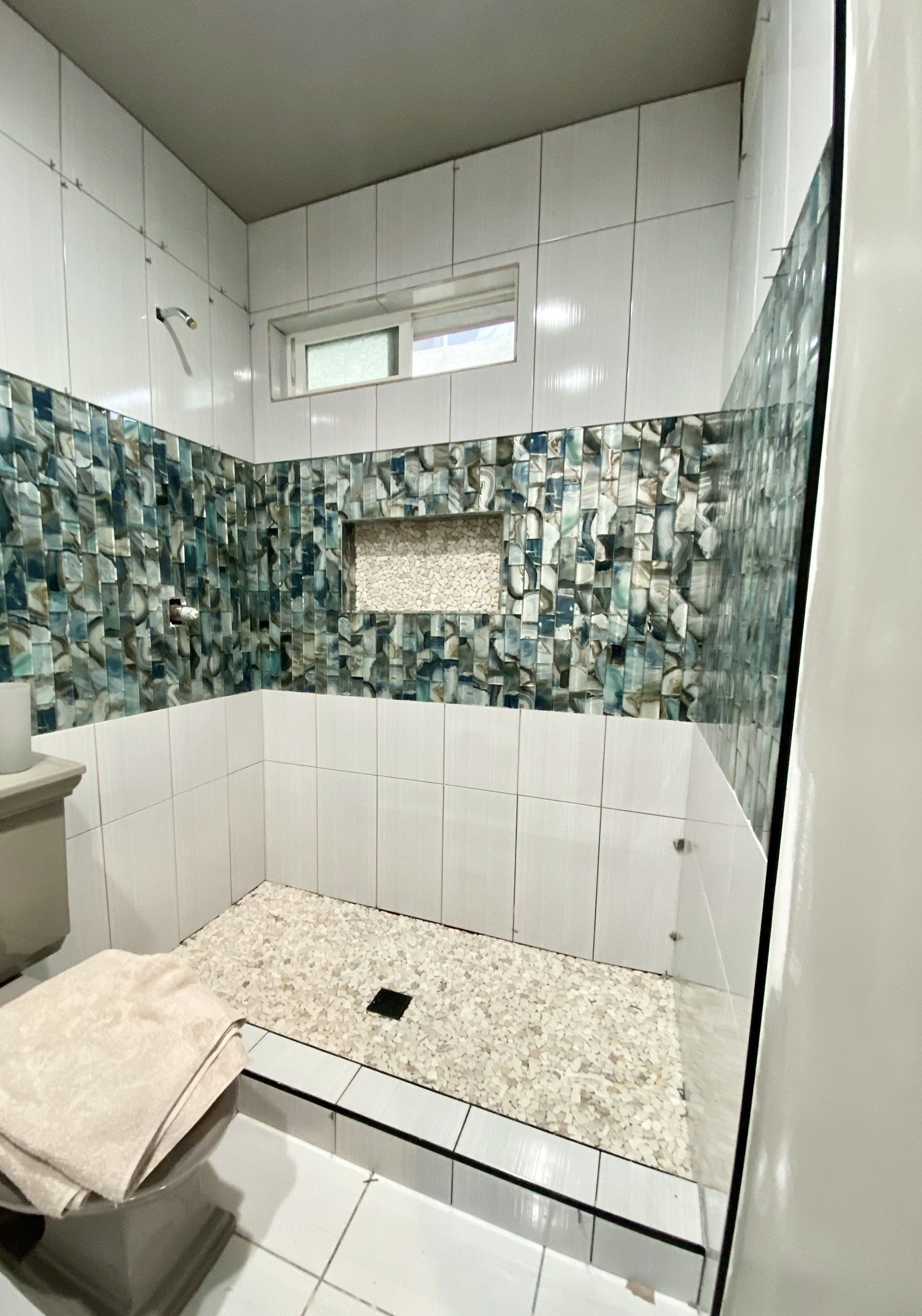 A bathroom with a walk in shower , toilet , sink and window.