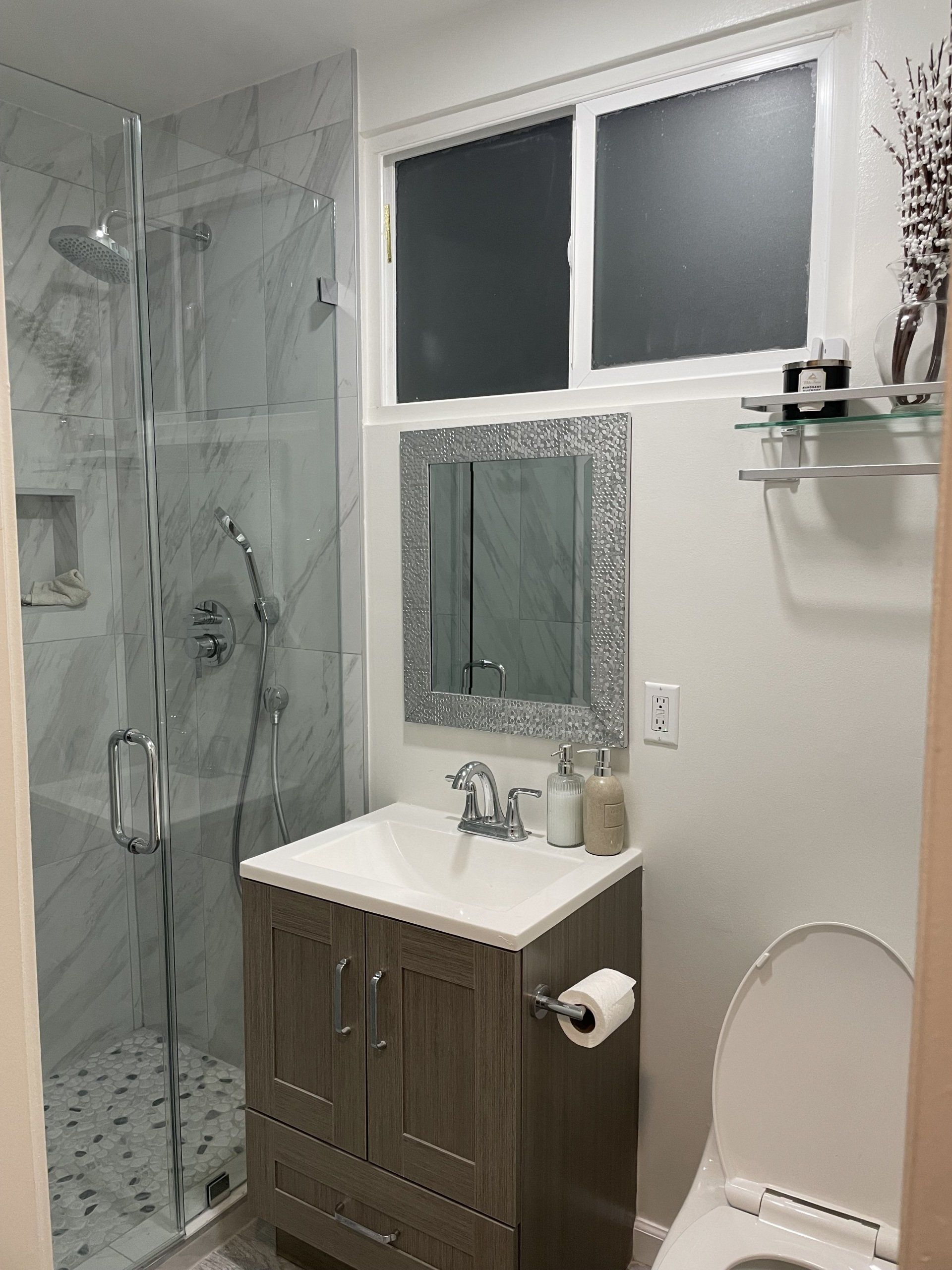 A bathroom with a sink , toilet , shower and mirror.