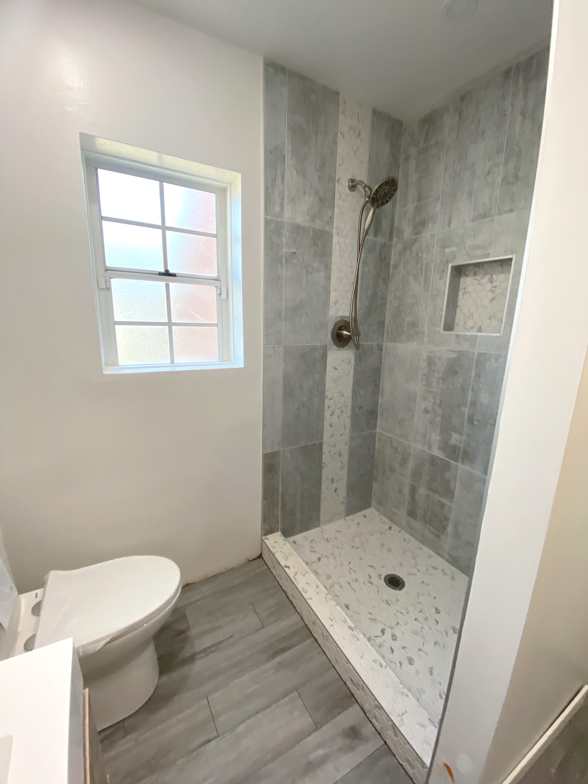 A bathroom with a toilet , shower and window.