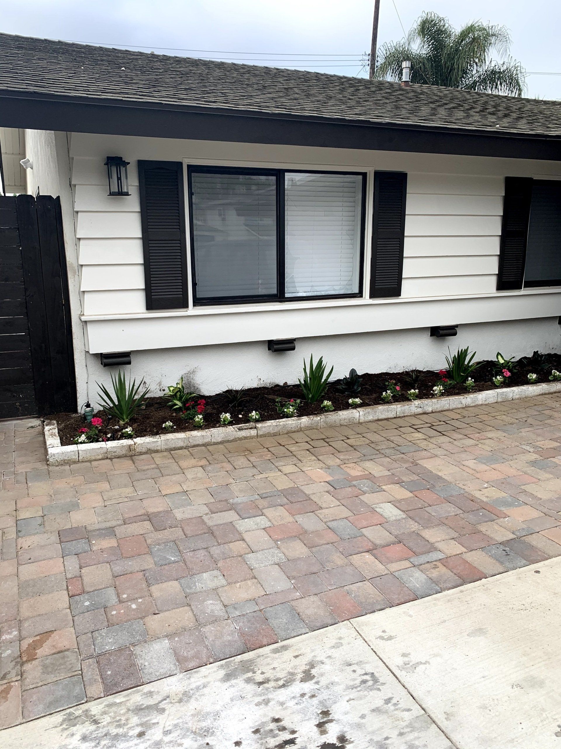 A white house with black shutters and a brick driveway