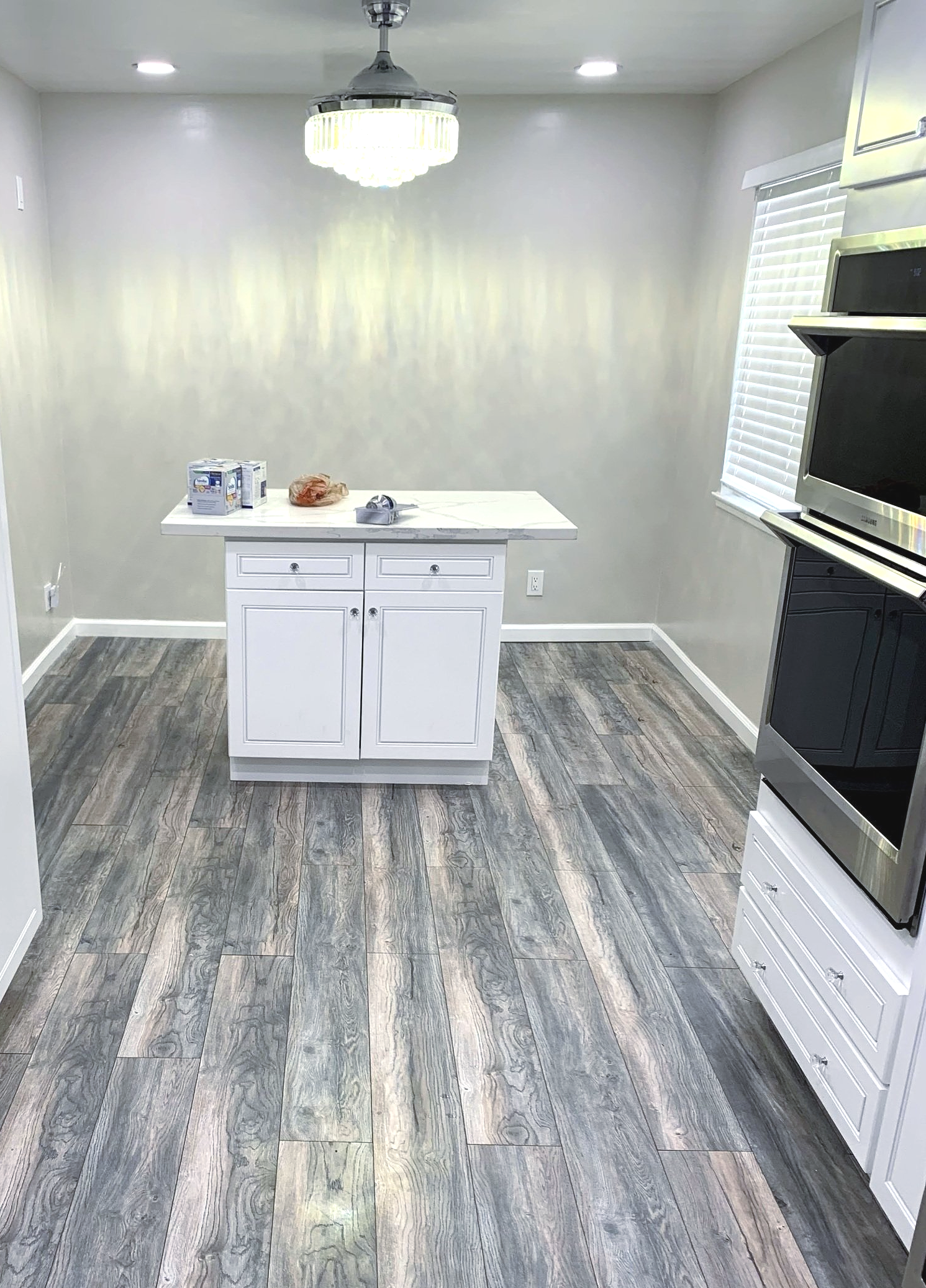 A kitchen with a wooden floor , white cabinets , and stainless steel appliances.