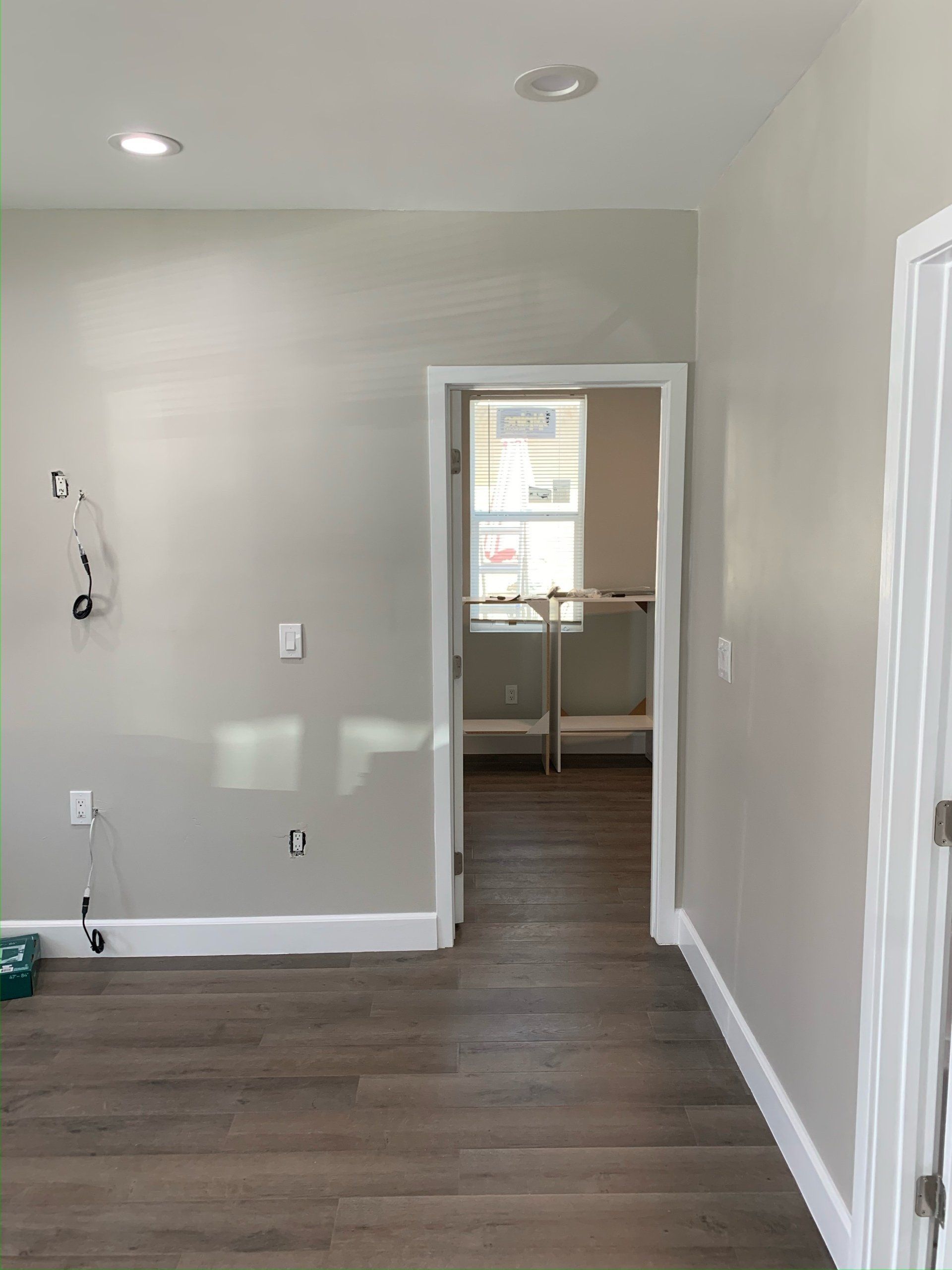 A hallway with hardwood floors and white trim leading to a bedroom.