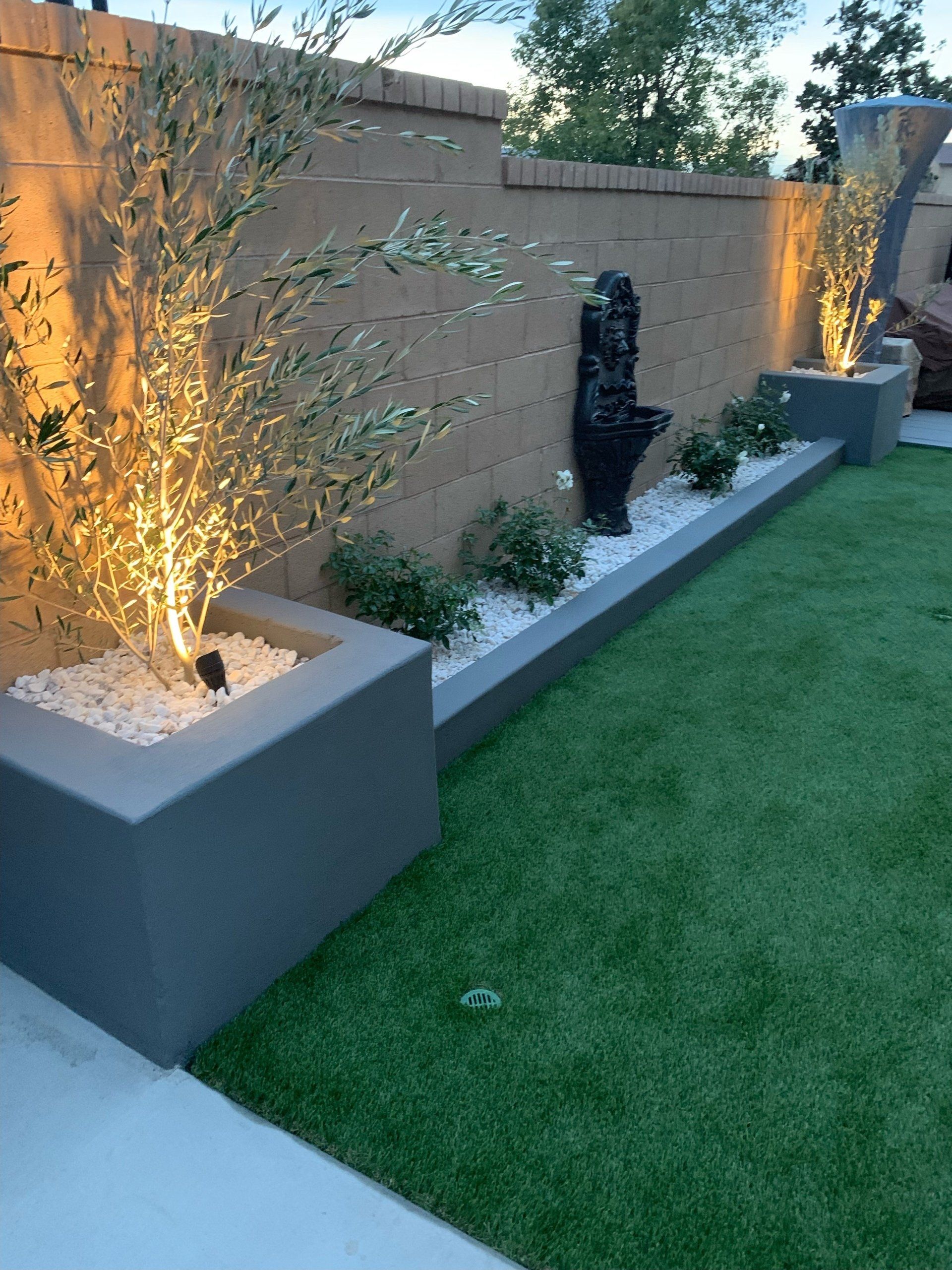 A backyard with a fence , planters , trees and a fountain.