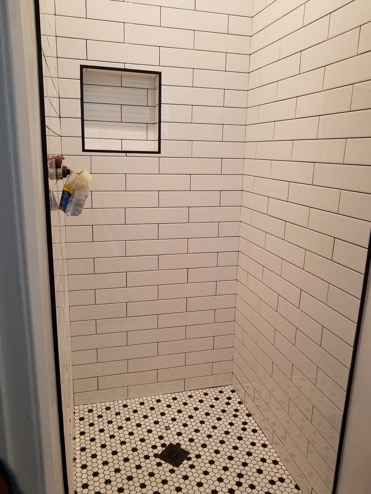 A shower with white tiles and black dots on the floor