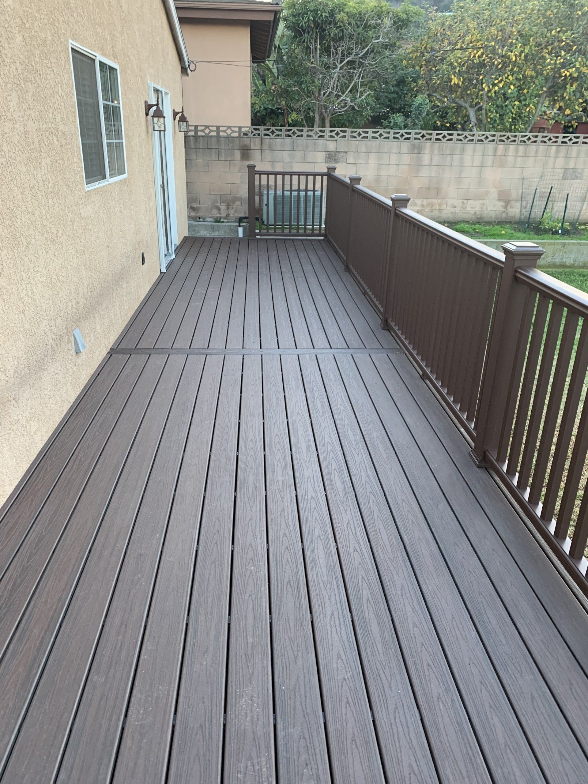A large wooden deck with a railing and a house in the background.