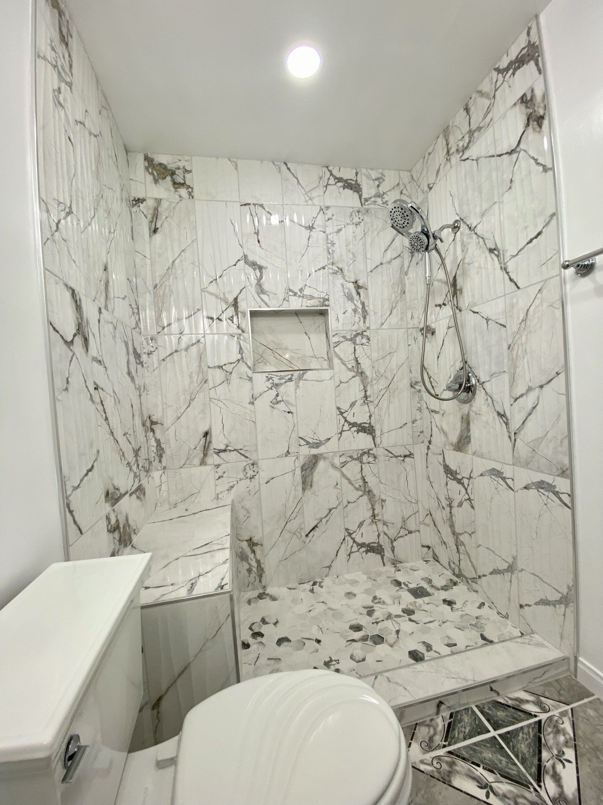 A bathroom with a toilet , shower and marble tiles.
