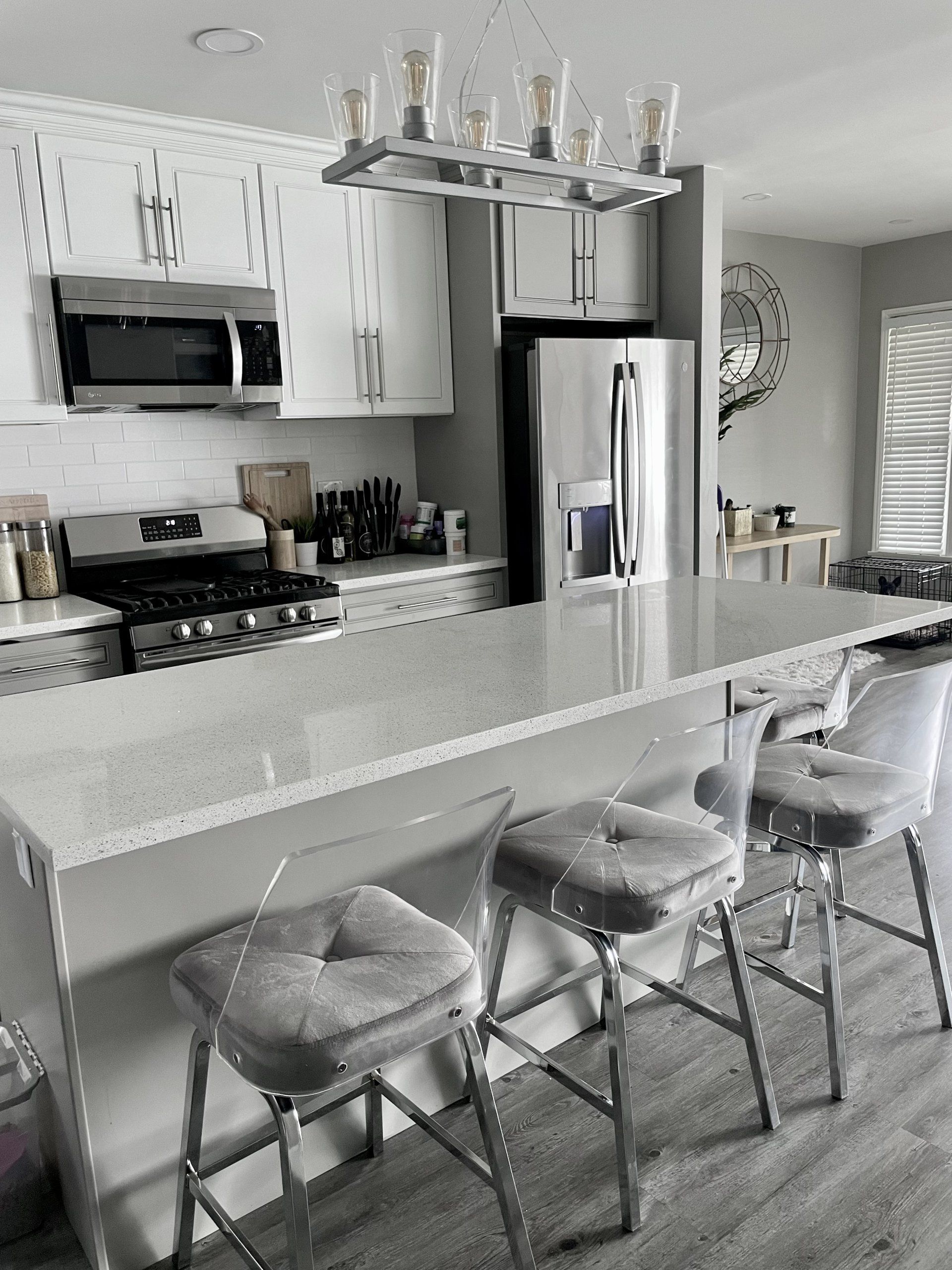A kitchen with white cabinets , a stove , a refrigerator , and a chandelier.